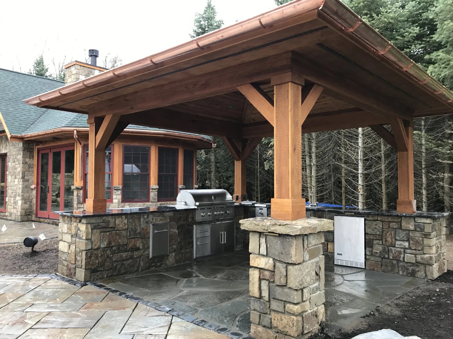 Outdoor living contractor Syracuse NY timber frame pavilion with stone columns and outdoor kitchen