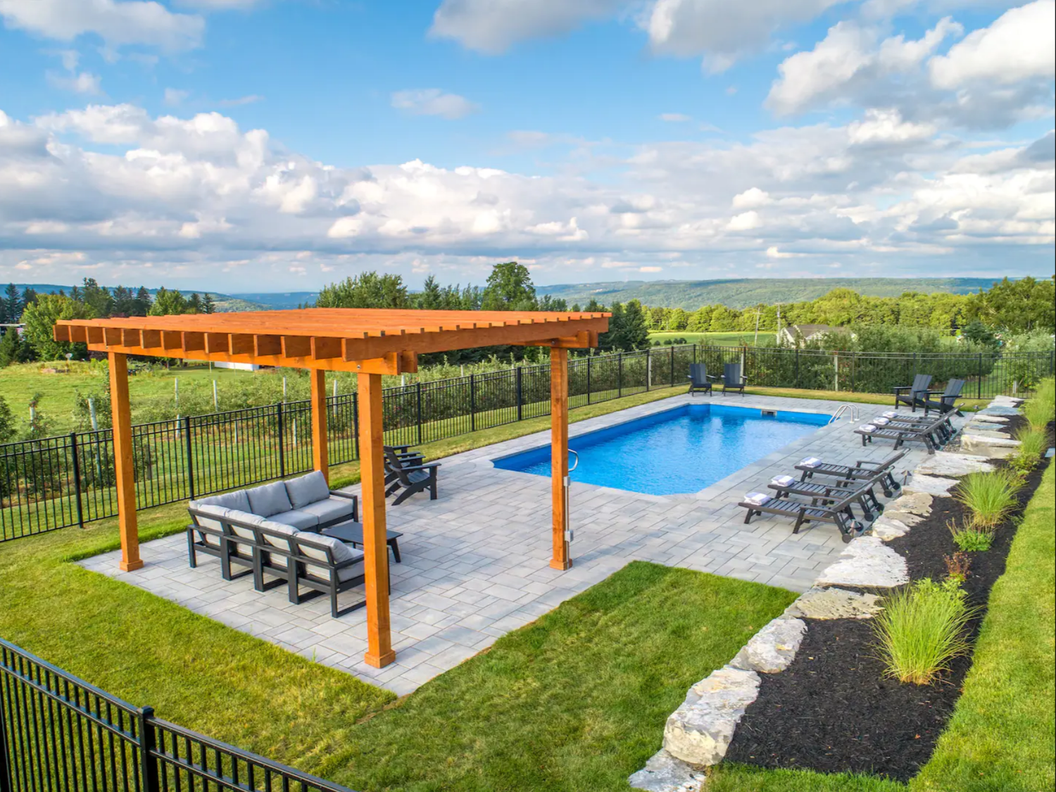 Backyard renovation Syracuse pergola and dining area beside an in-ground pool with water view