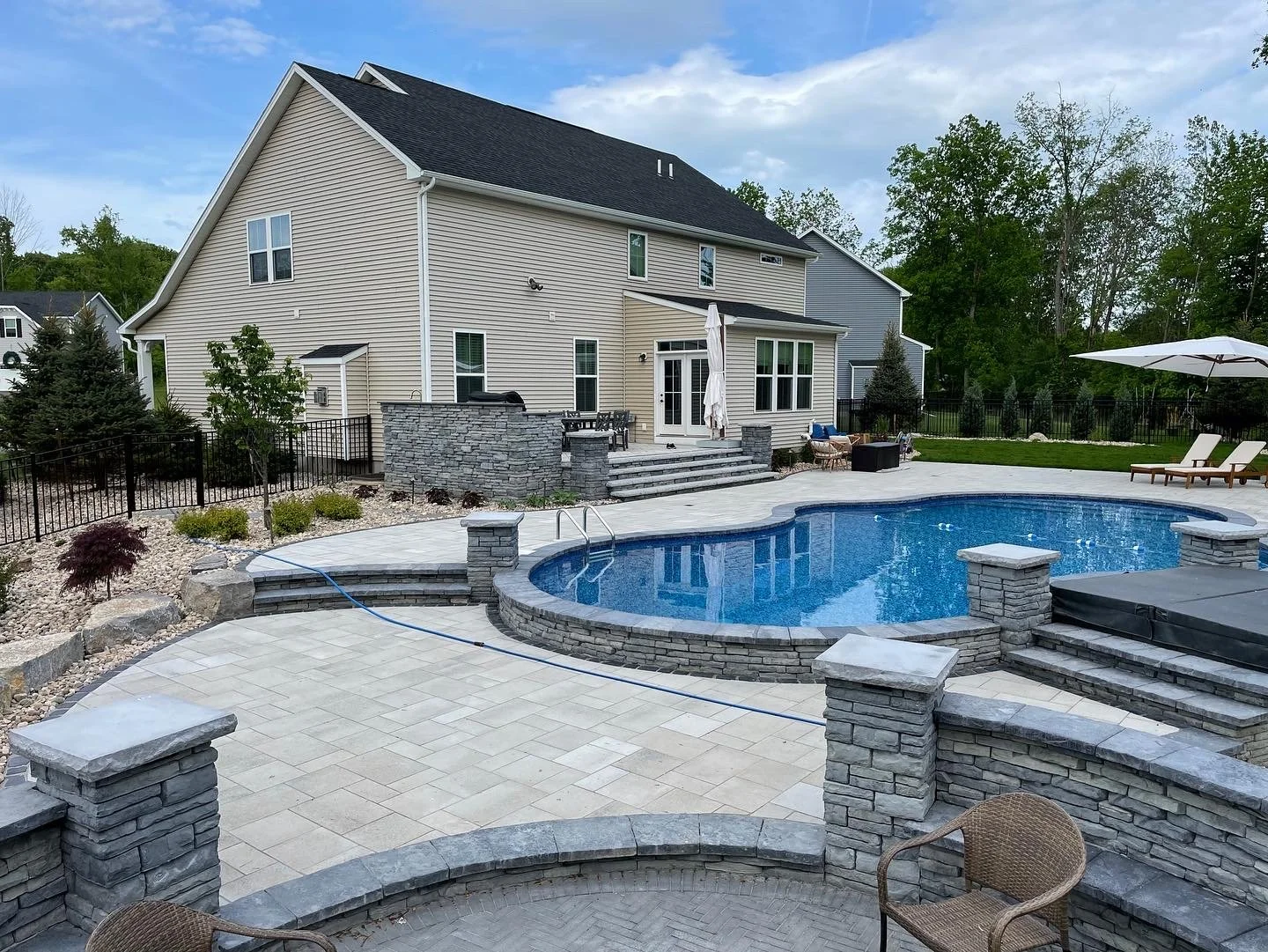 Backyard with a swimming pool, pool deck, lounge chairs, patio furniture, and a two-story house in the background.