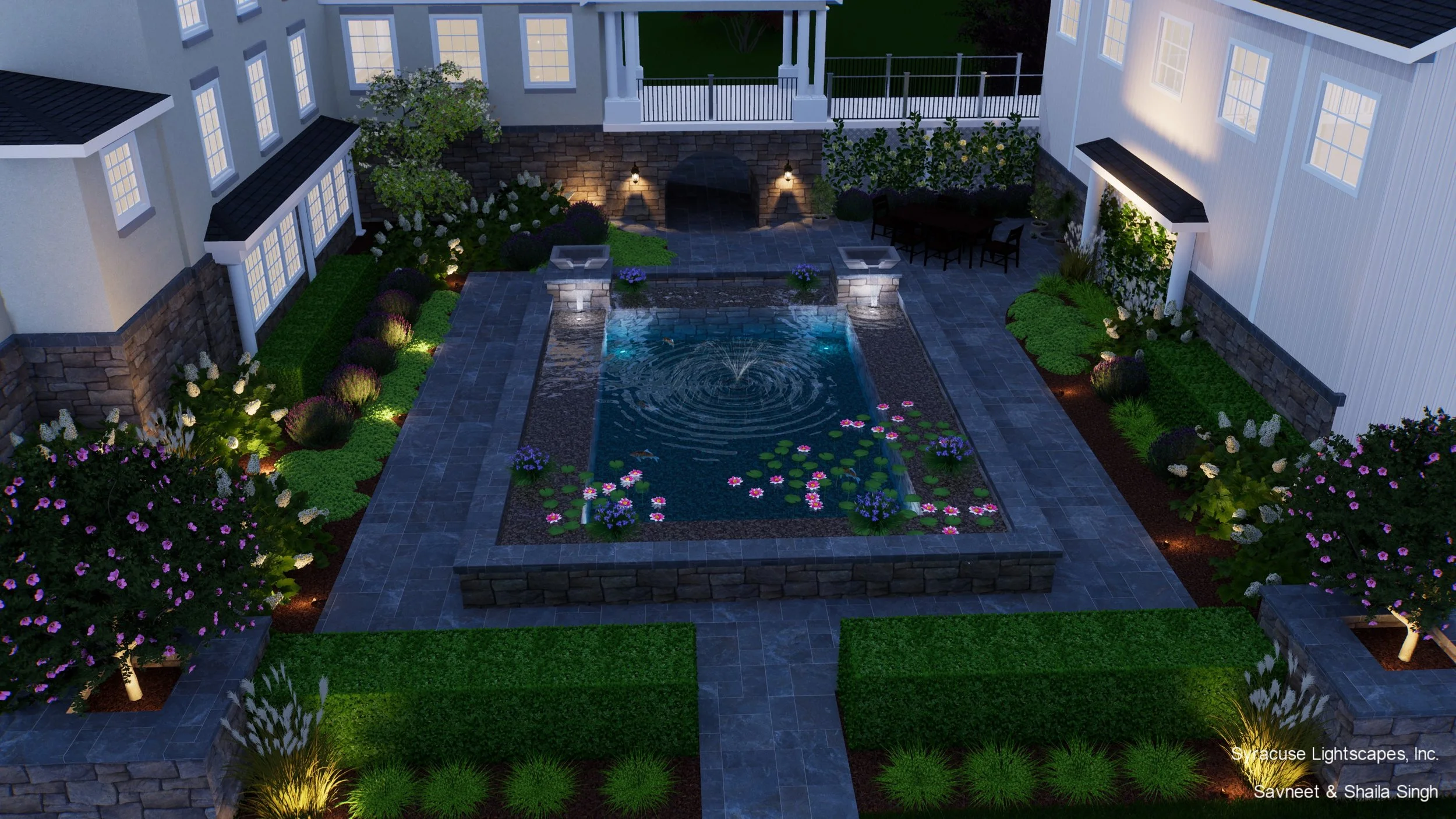 Nighttime view of a backyard with a rectangular fountain in the center, surrounded by landscaped garden beds with trees, bushes, and flowers, lit by outdoor lighting, with neighboring white houses and a patio with outdoor furniture.