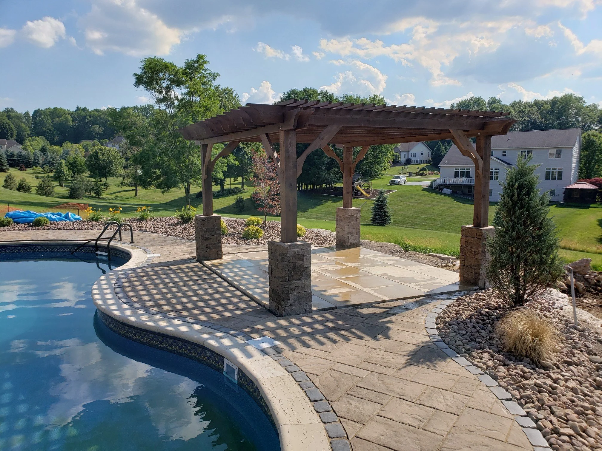 Residential backyard with a swimming pool and a wooden gazebo under a clear sky.