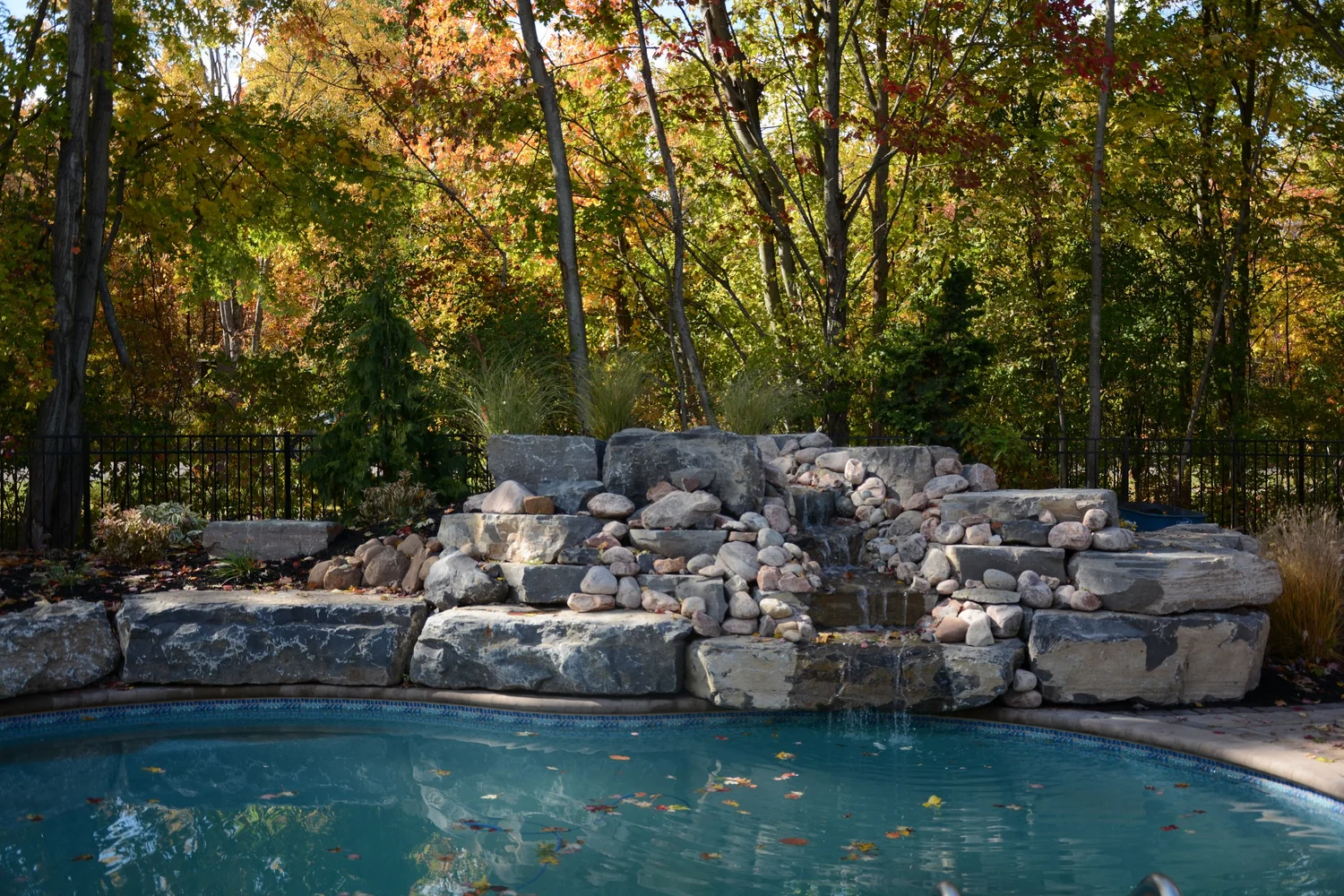 Pool waterfall installation Syracuse NY with natural stone boulders and landscaping