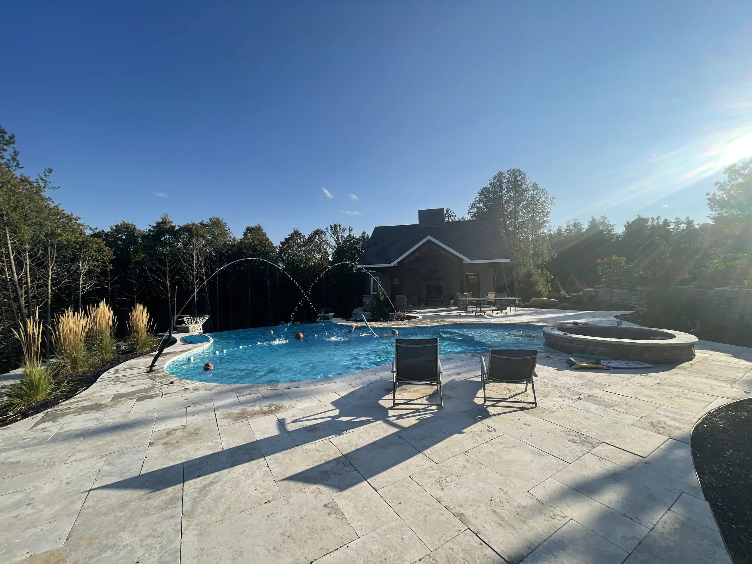 Backyard with a swimming pool, lounge chairs, a hot tub, and a small shed, under a clear blue sky with the sun shining brightly.