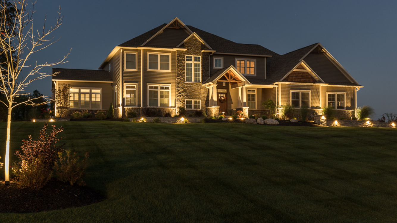 A large, well-lit two-story house with a landscaped yard at night