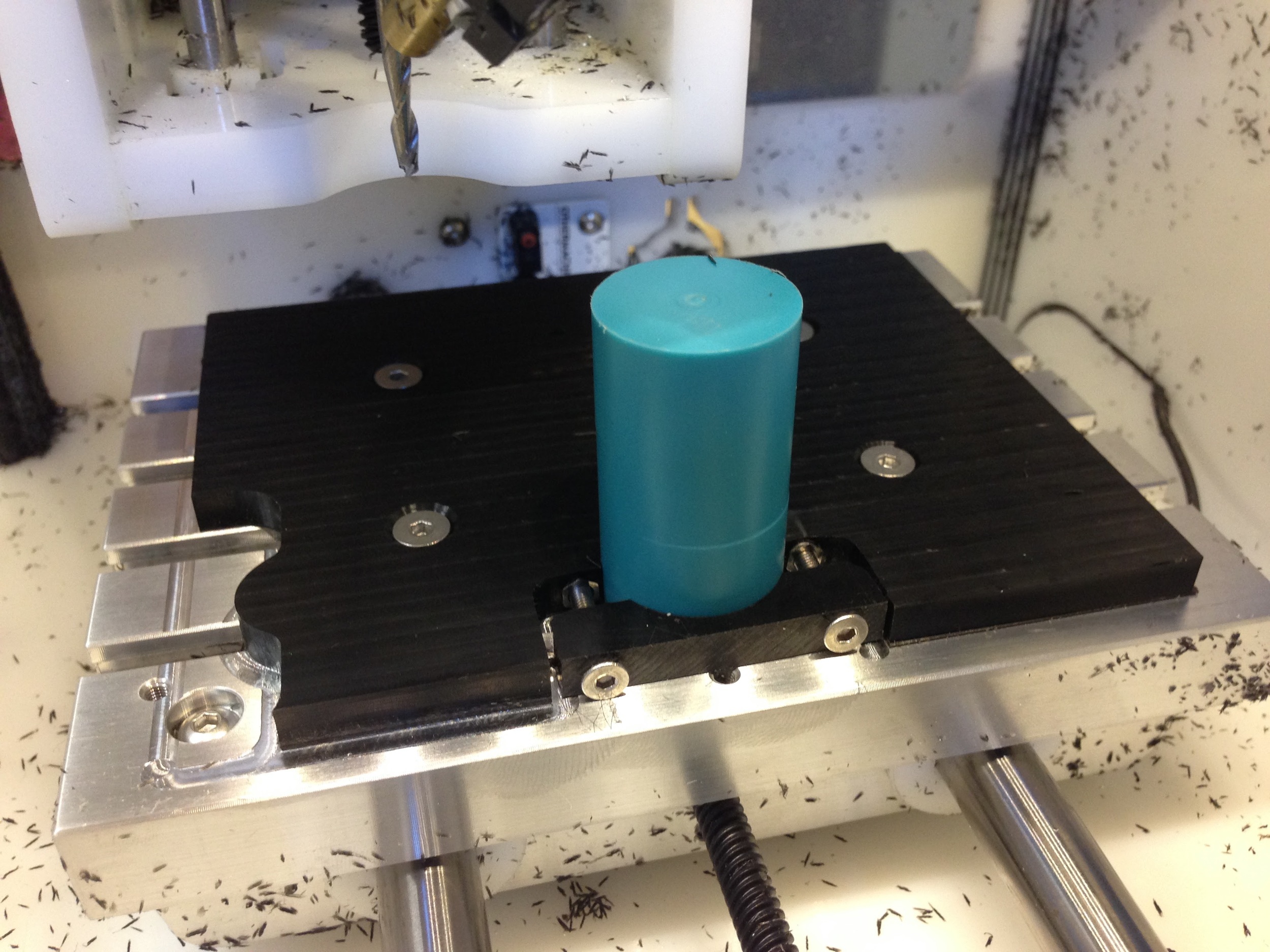 The original stock in place. I did cut it off on the lathe and do a face cut on the bottom side before milling, so it sat flat on the Othermill's t-slot bed. Both the fixturing plate and stock are Delrin. 