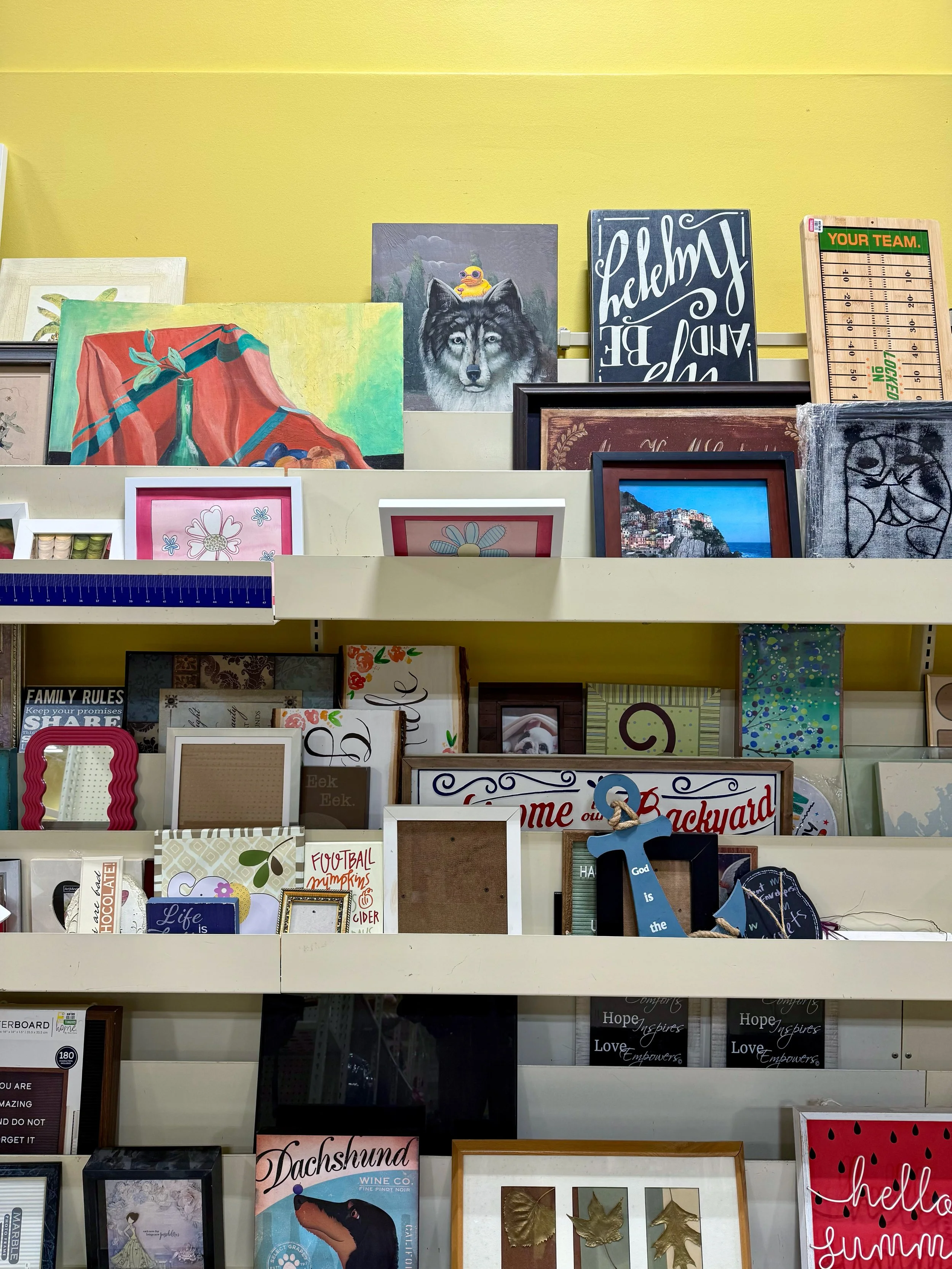 Paintings stacked in racks in front of a yellow wall.