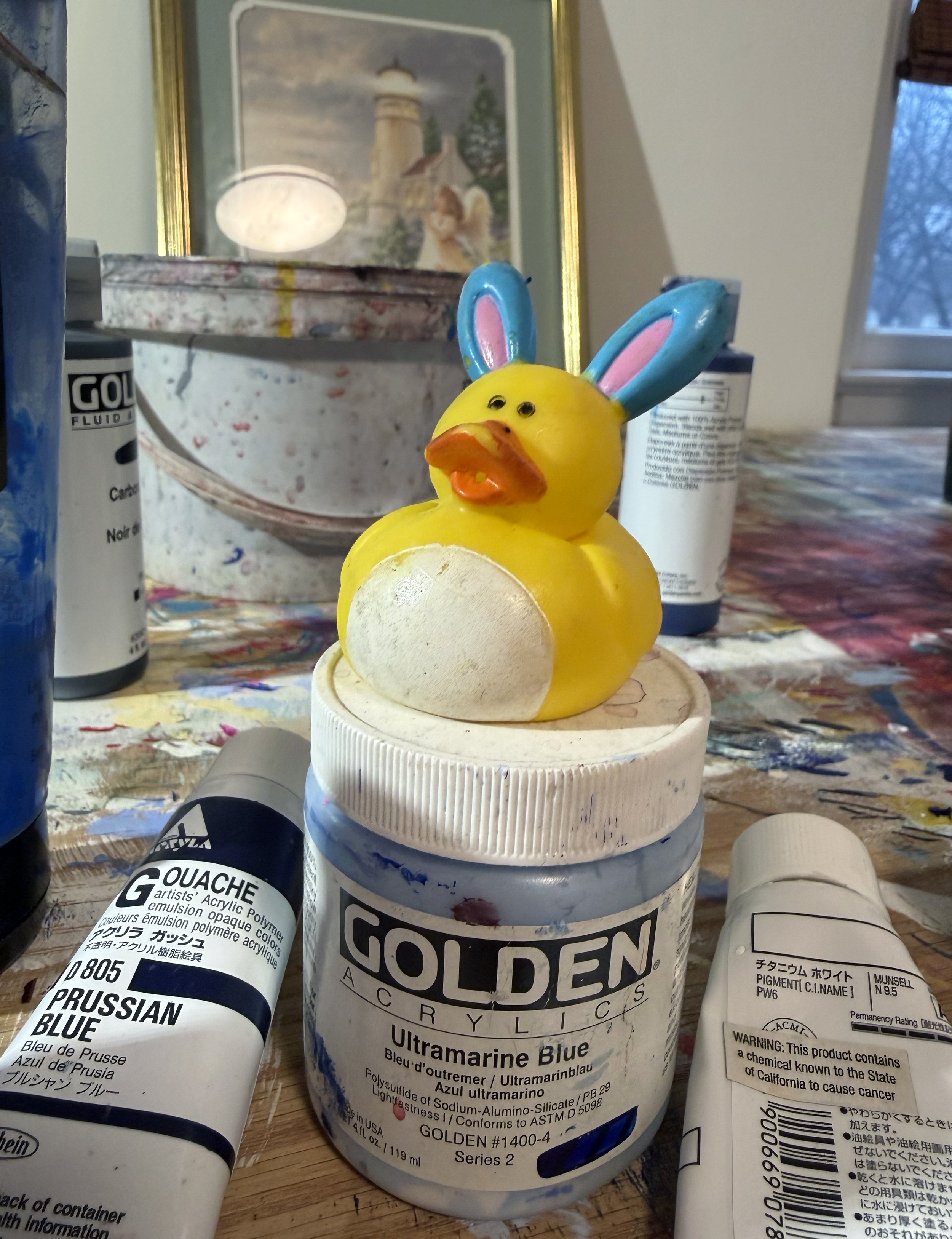 Yellow rubber duck toy wearing blue bunny ears resting on a paint container.