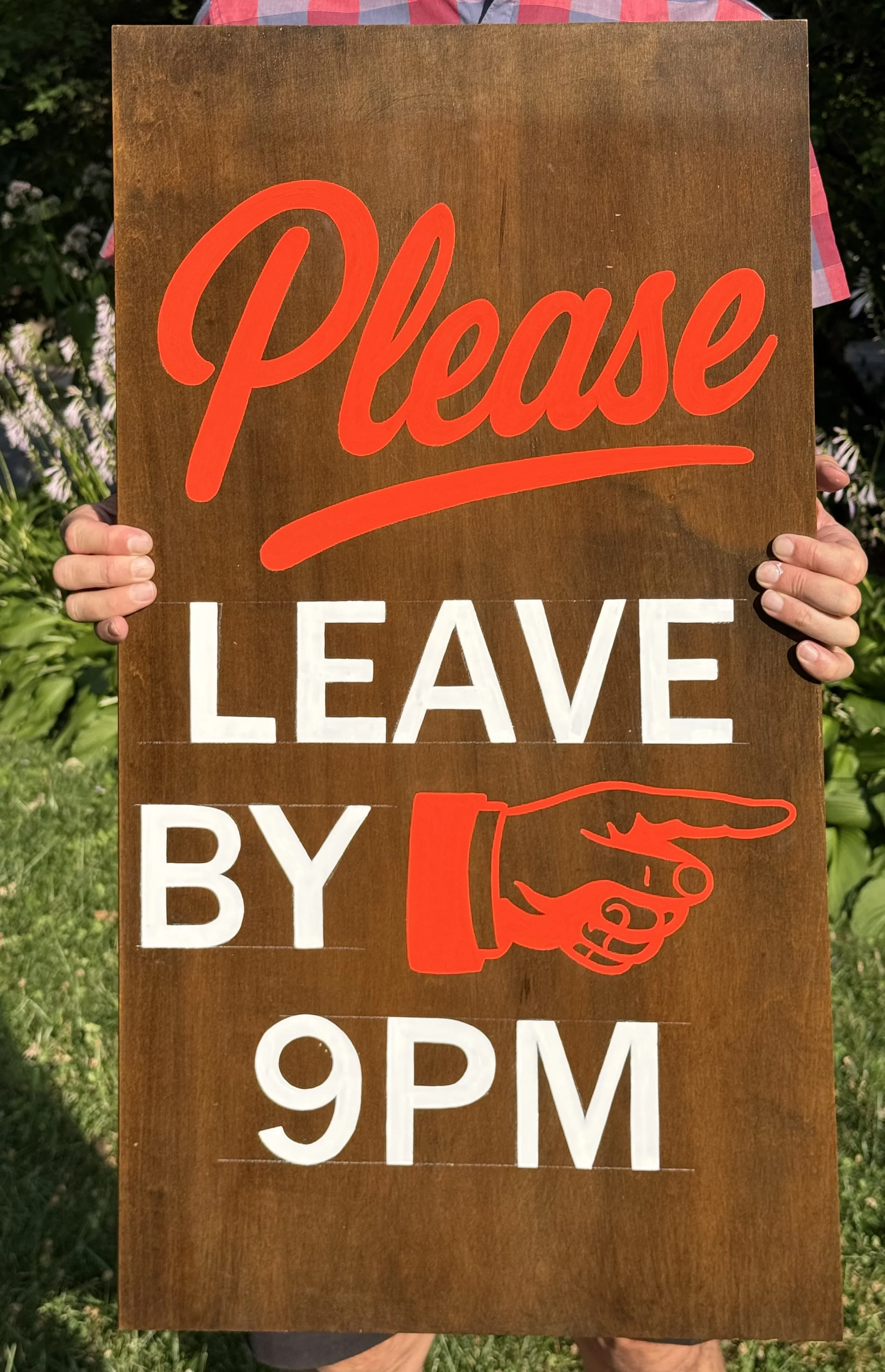 Person holding a painted sign on a piece of wood that says, Please leave by 9pm