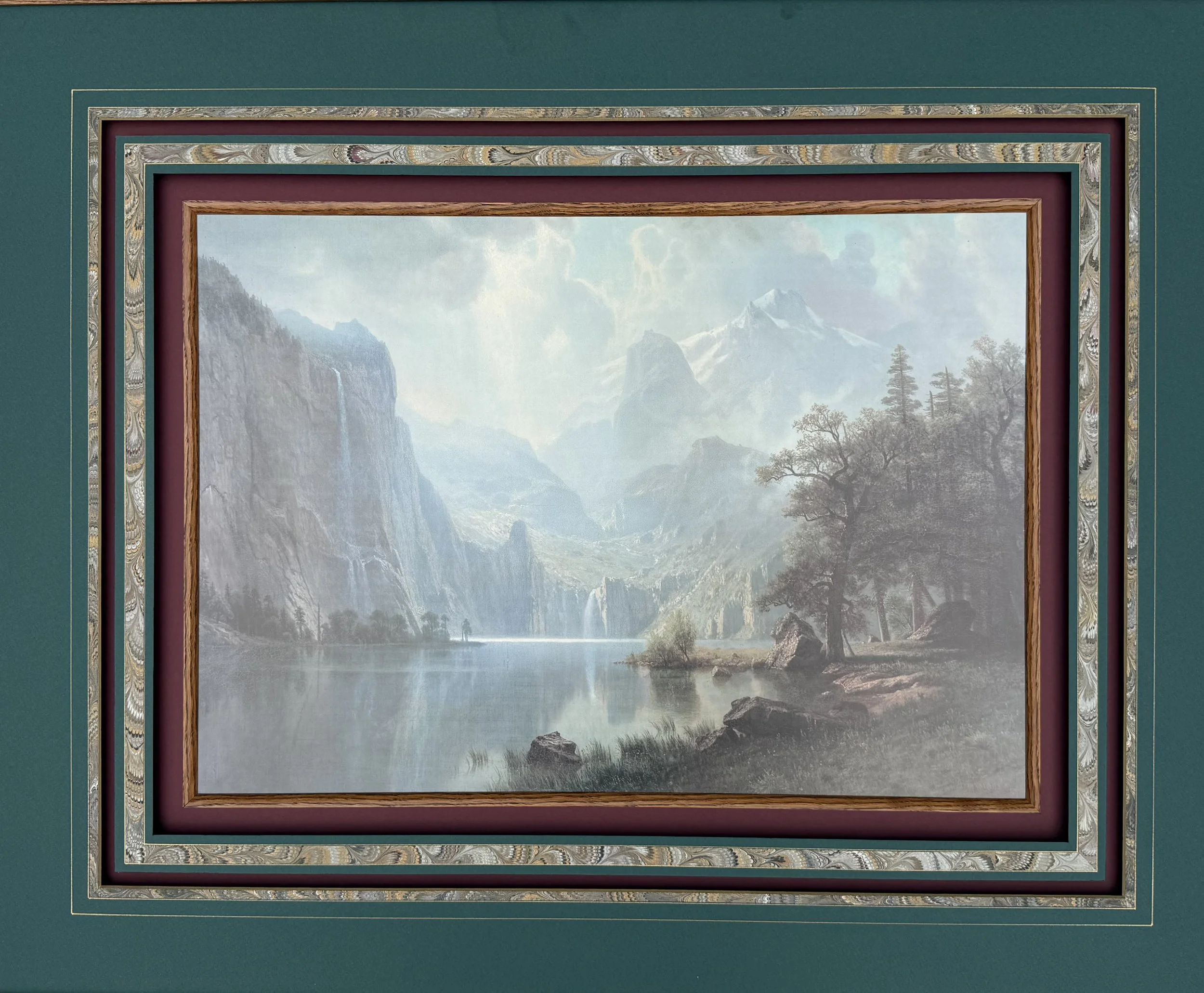A green framed painting of a majestic mountainous landscape.