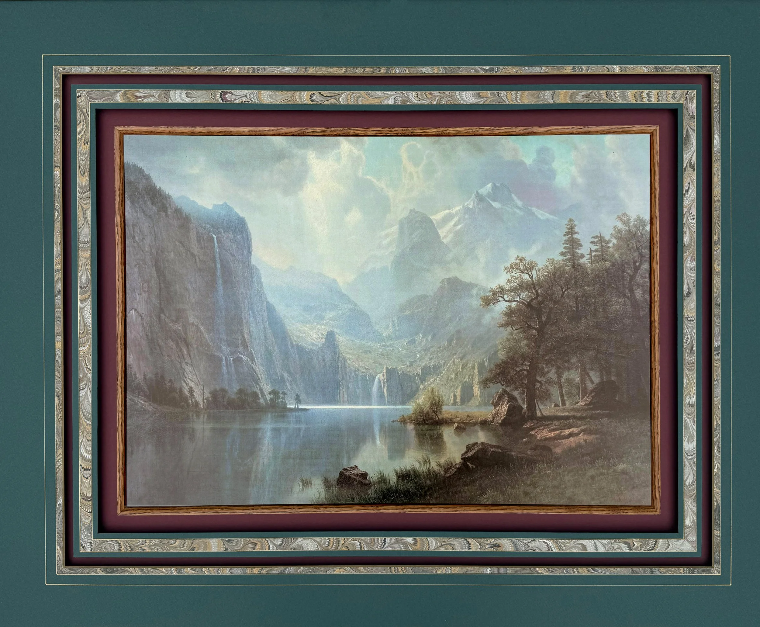 A painting with a green frame of a monumental mountainous landscape with waterfalls, tranquil river, and trees.