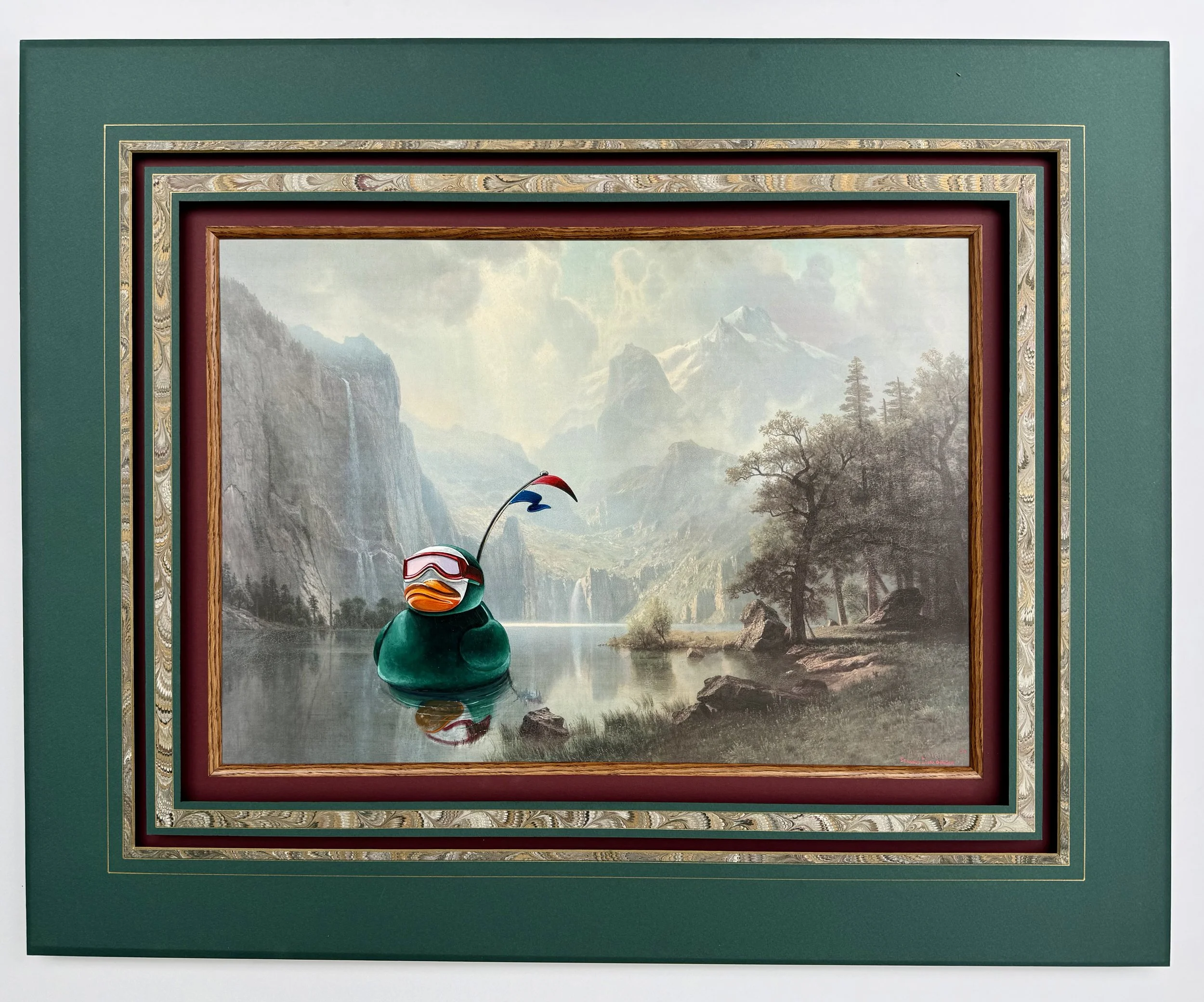 A painting with a green frame of a large green rubber duck with goggles floating in a lake surrounded by mountains and wilderness.