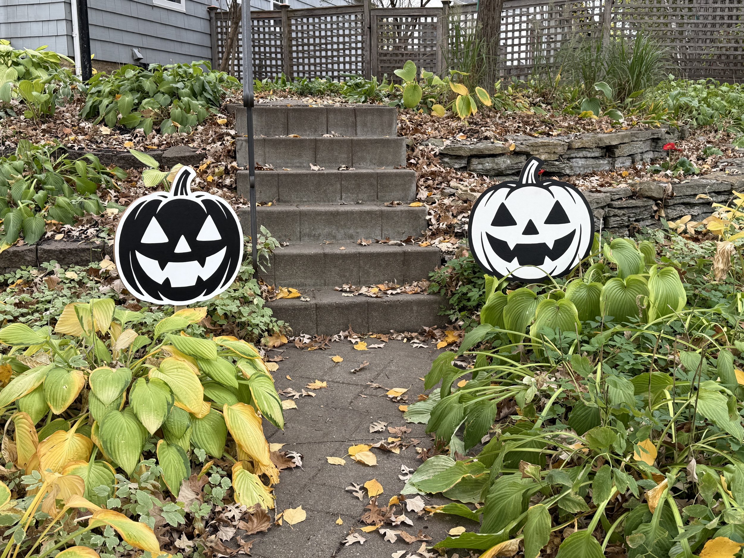 Two black and white pumpkin signs yard decor by outside steps.