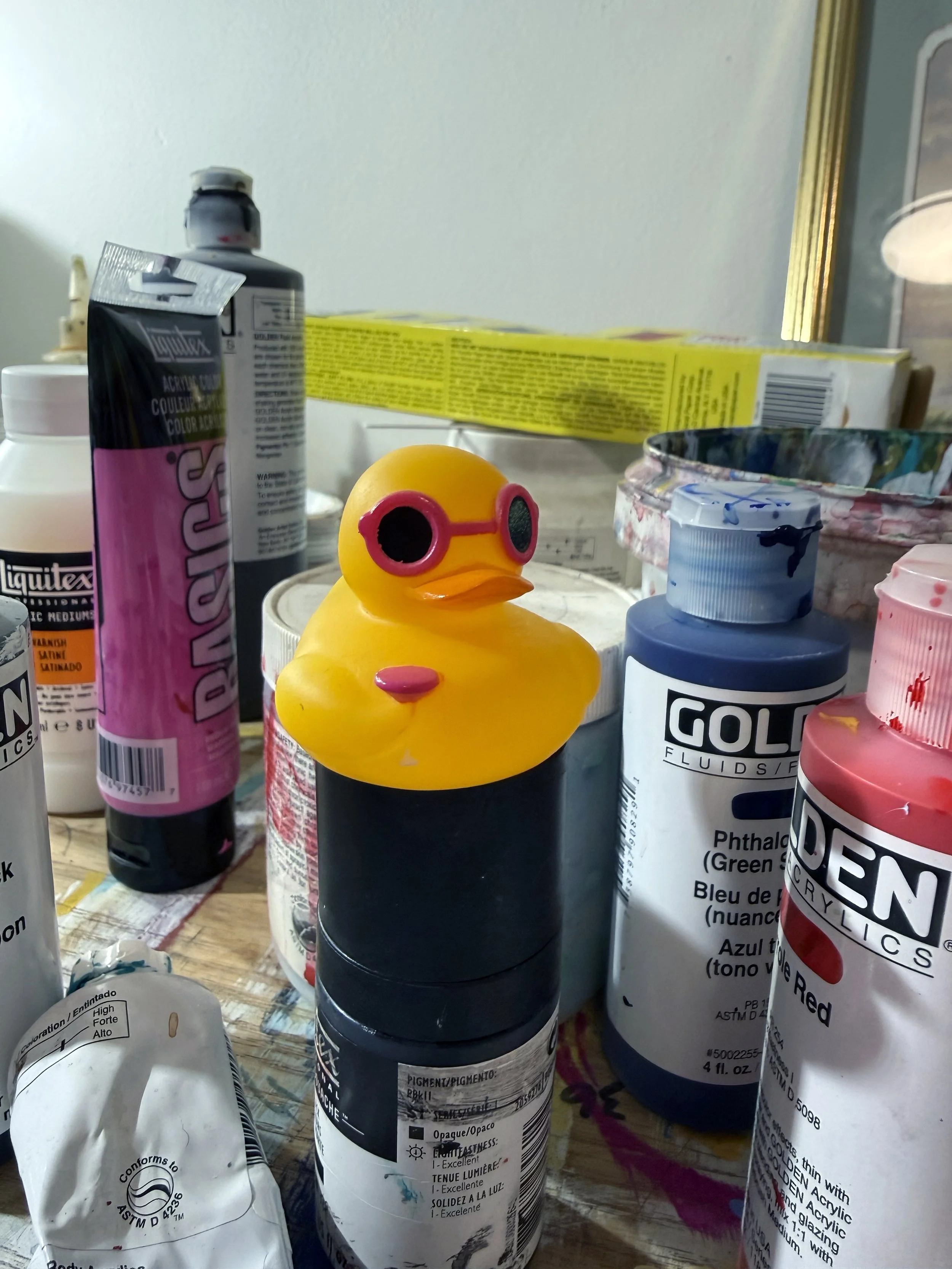 Small yellow rubber duck toy  on a paint bottle that is wearing pink sunglasses and holding a pink martini glass
