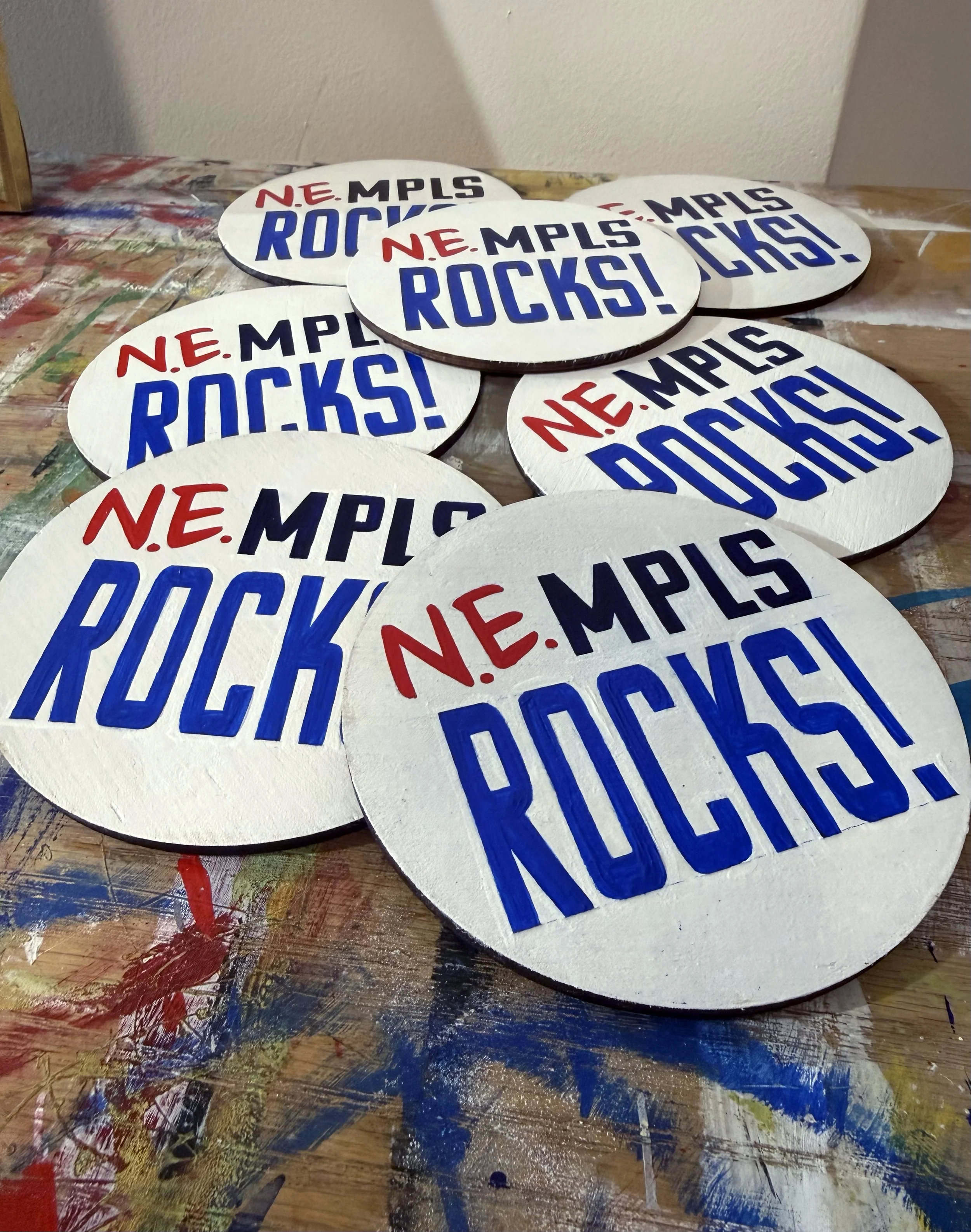 A pile of white circles on a table, with text on them that reads, 'NE MPLS ROCKS!' in red and blue lettering.