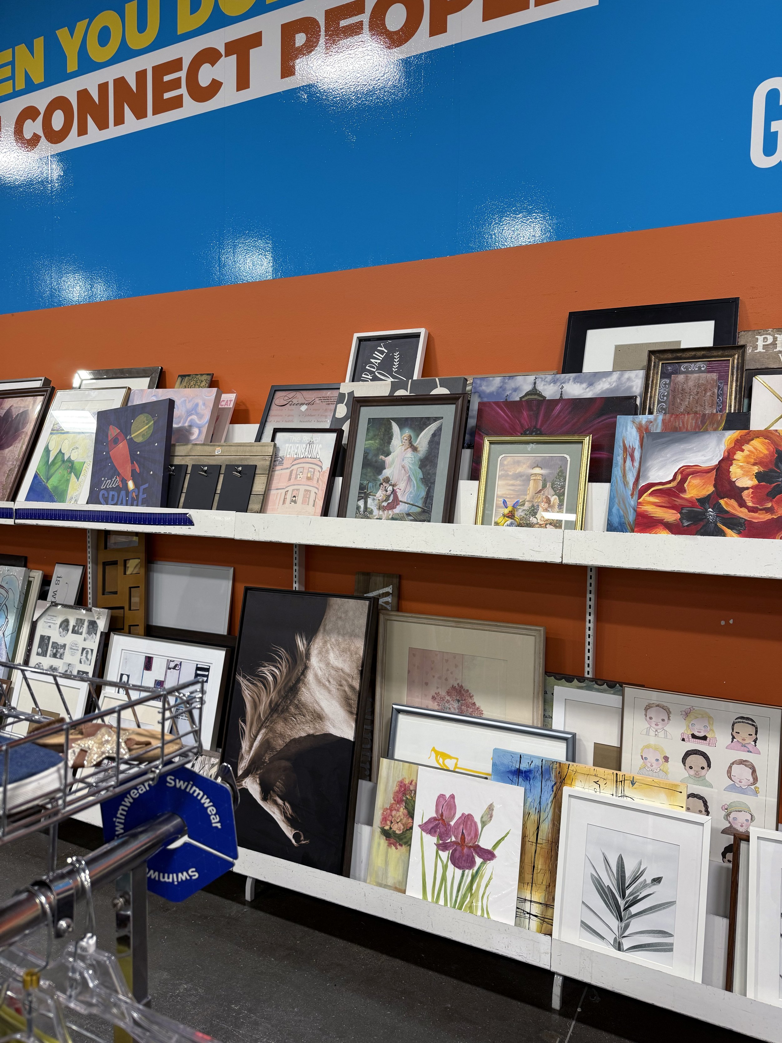 A number of framed paintings stacked on a shelf in a store.
