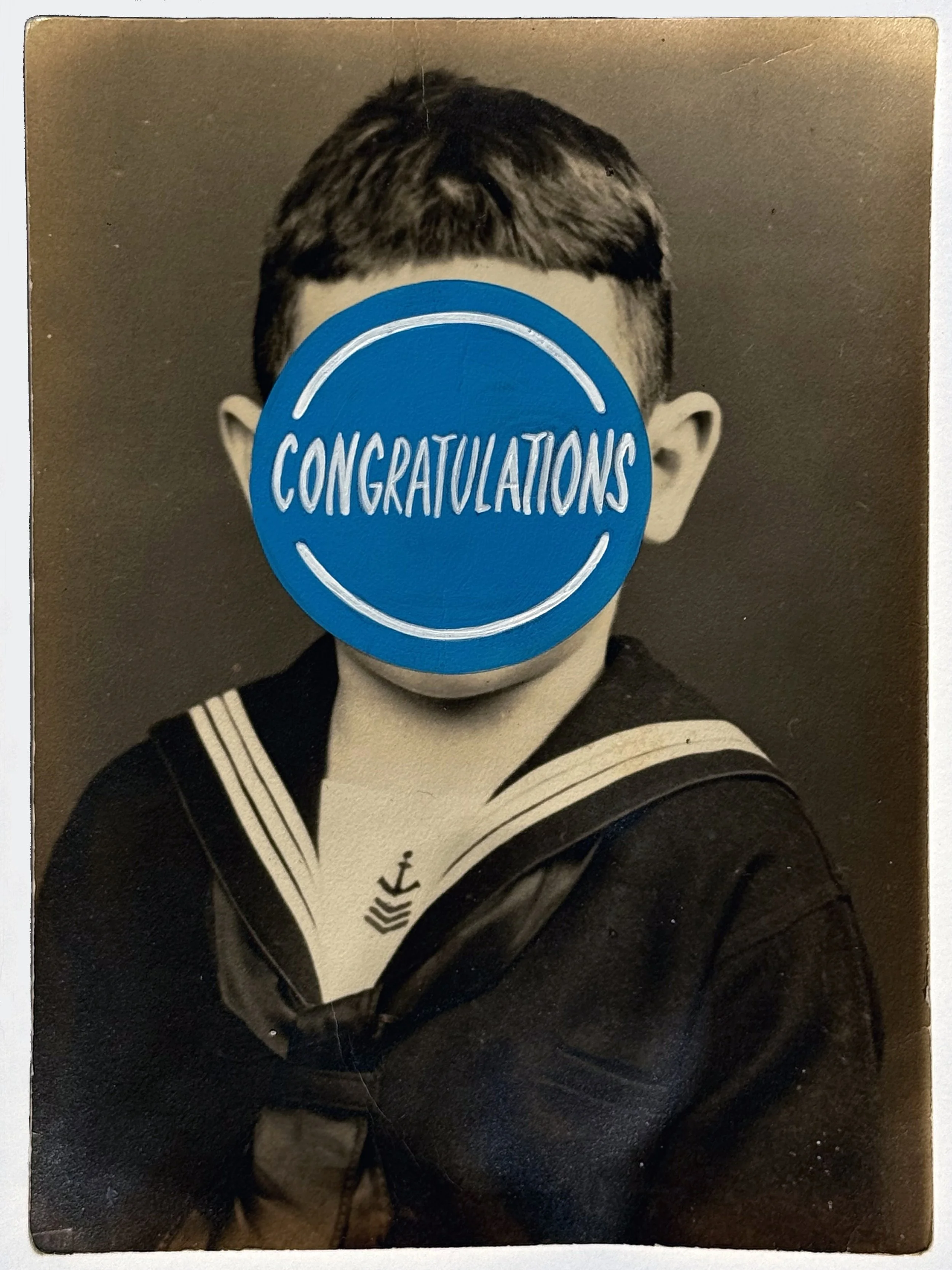 Old portrait photograph of a boy with a blue dot painted on his face with the word Congratulations painted on top.