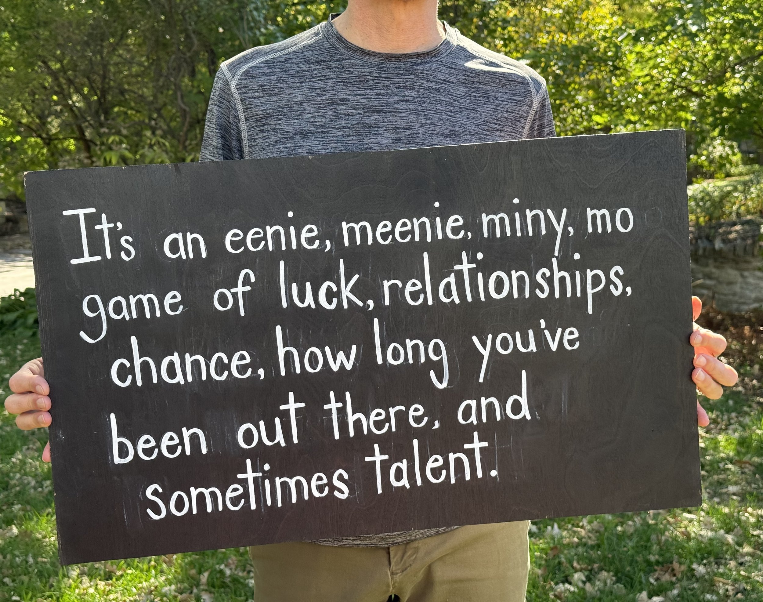 Man holding a hand painted outside that says eenie, meenie, miny, mo