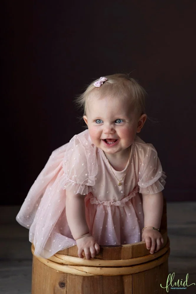 One year old smiling standing in a basket.