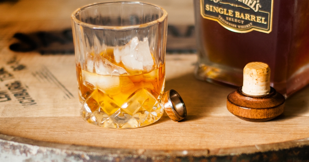 Whiskey barrel wood wedding ring. Wedding ring detail shot set on a whiskey barrel next to a glass of whiskey.