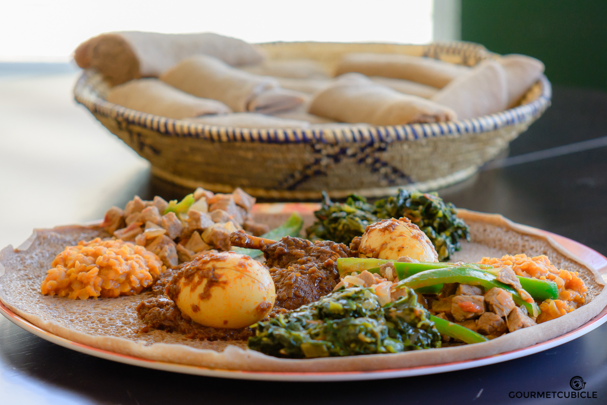 Misir Wot (lentils stew), Doro Wot (chicken stew), Gomen (Ethiopian collard green) and Beef Tibs served on injera bread.