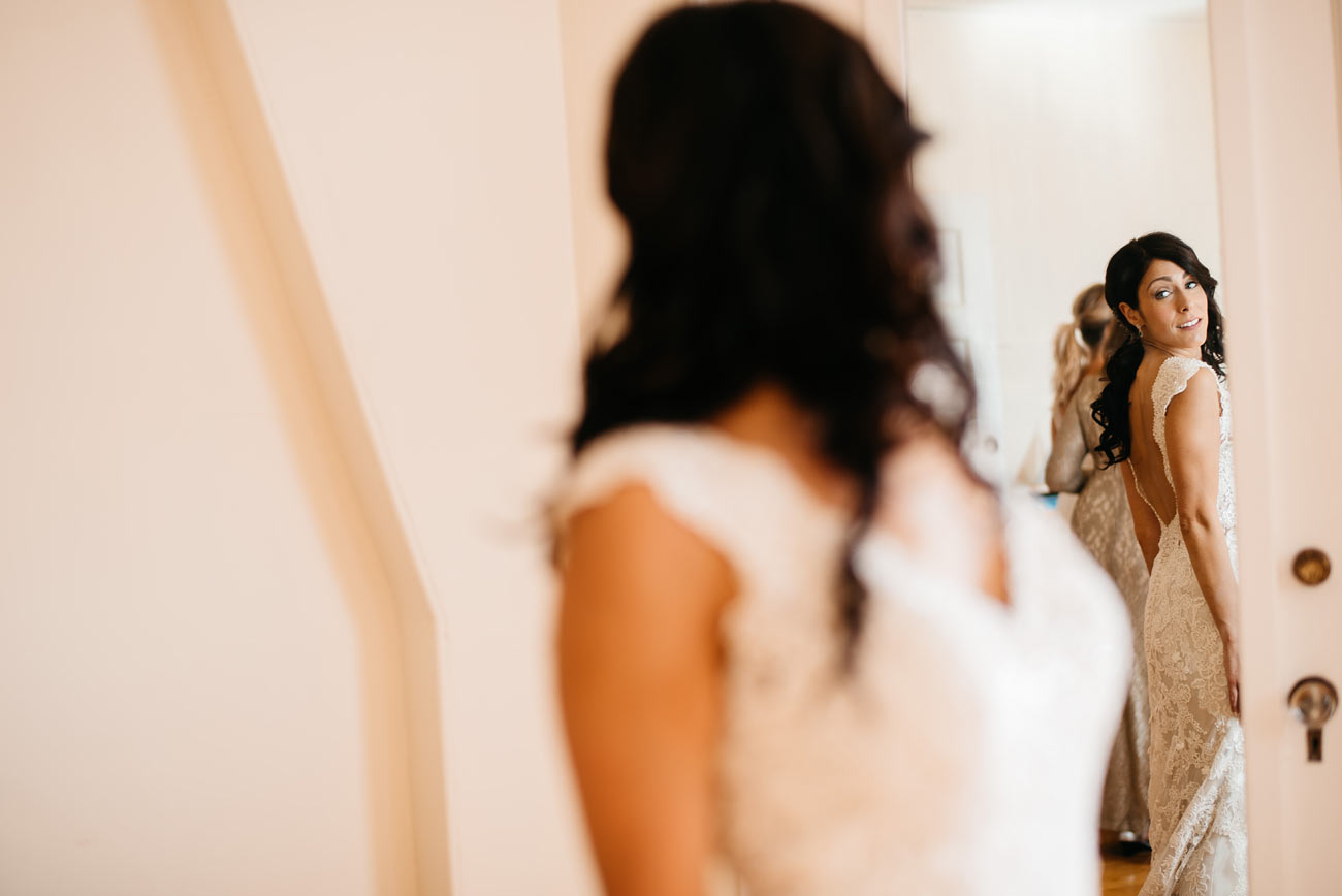 bride looking in mirror at the eastern point yacht club getting ready for her diy stylish outdoor wedding in gloucestor