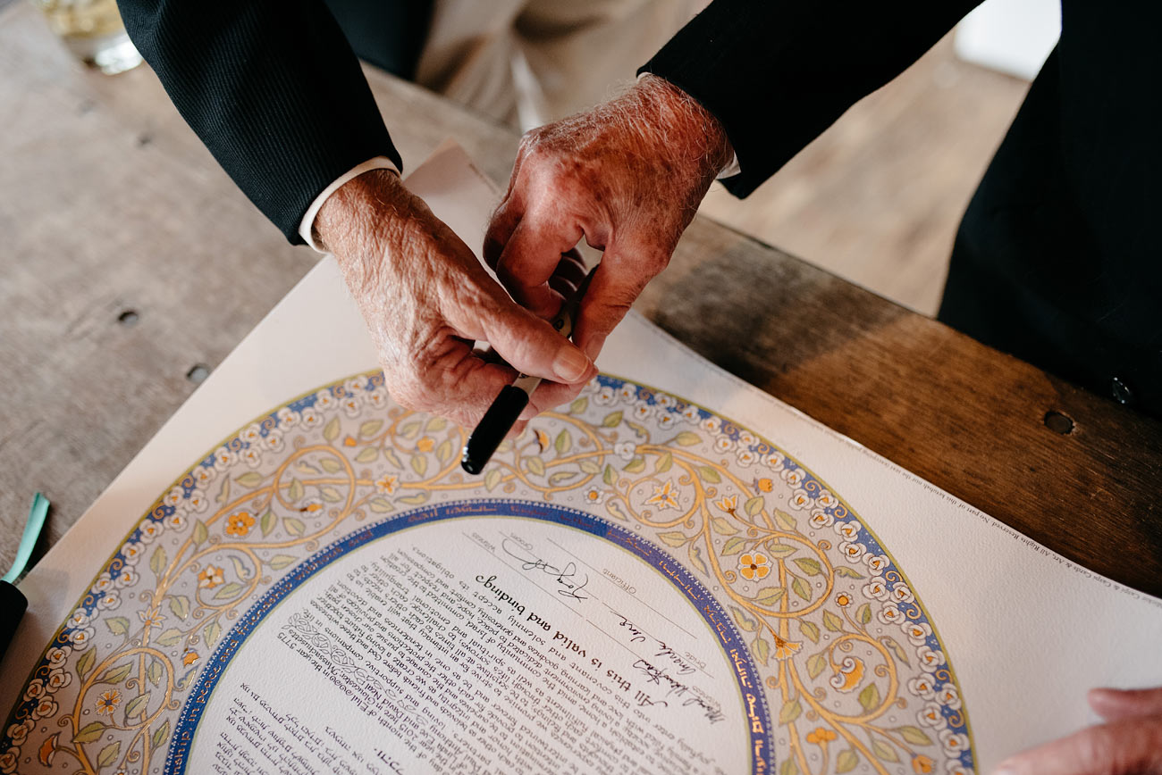 grandparents exchanging pens while signing a ketubah