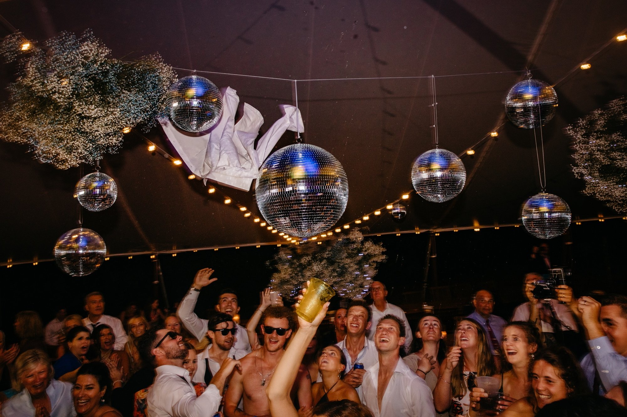 groom throws shirt in the air at a wedding reception with disco balls at chatham ma