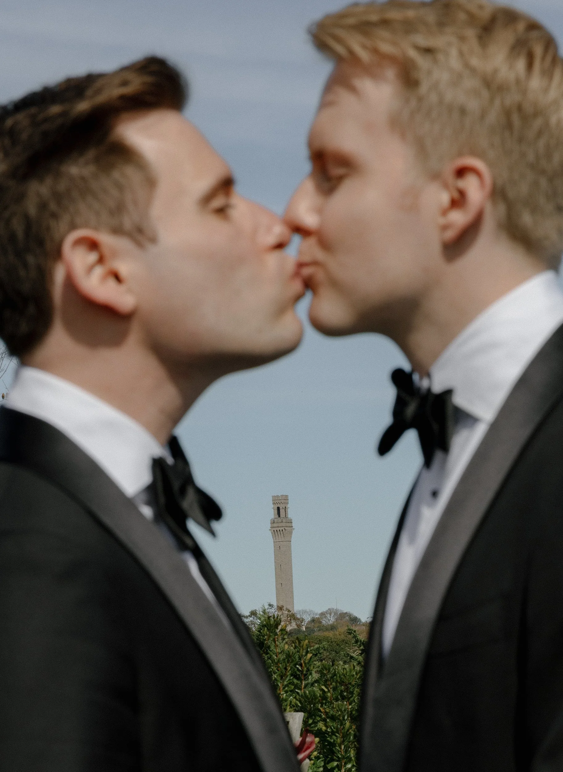 two same sex grooms kissing with pilgrim monument in the background 