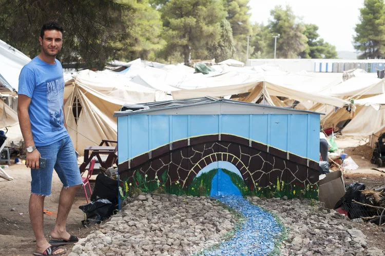 Jason with one of his artwork, brightening up Ritsona Camp. Photograph/Ann Eswein
