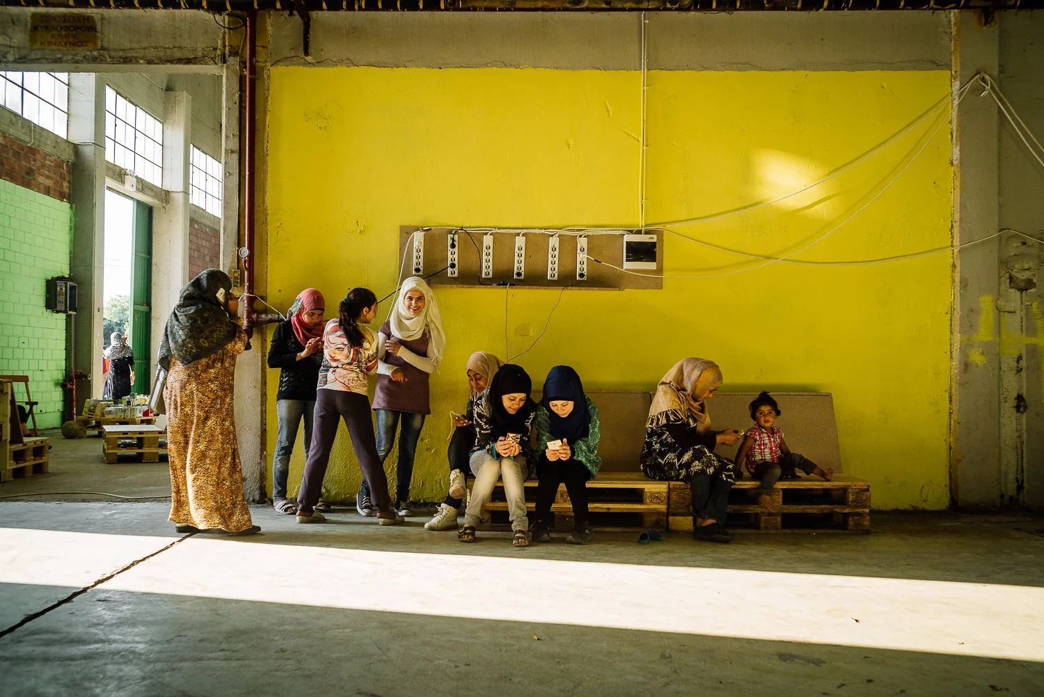 Young women charging their phones while testing out the wifi. Sindos Camp, Greece, 2016