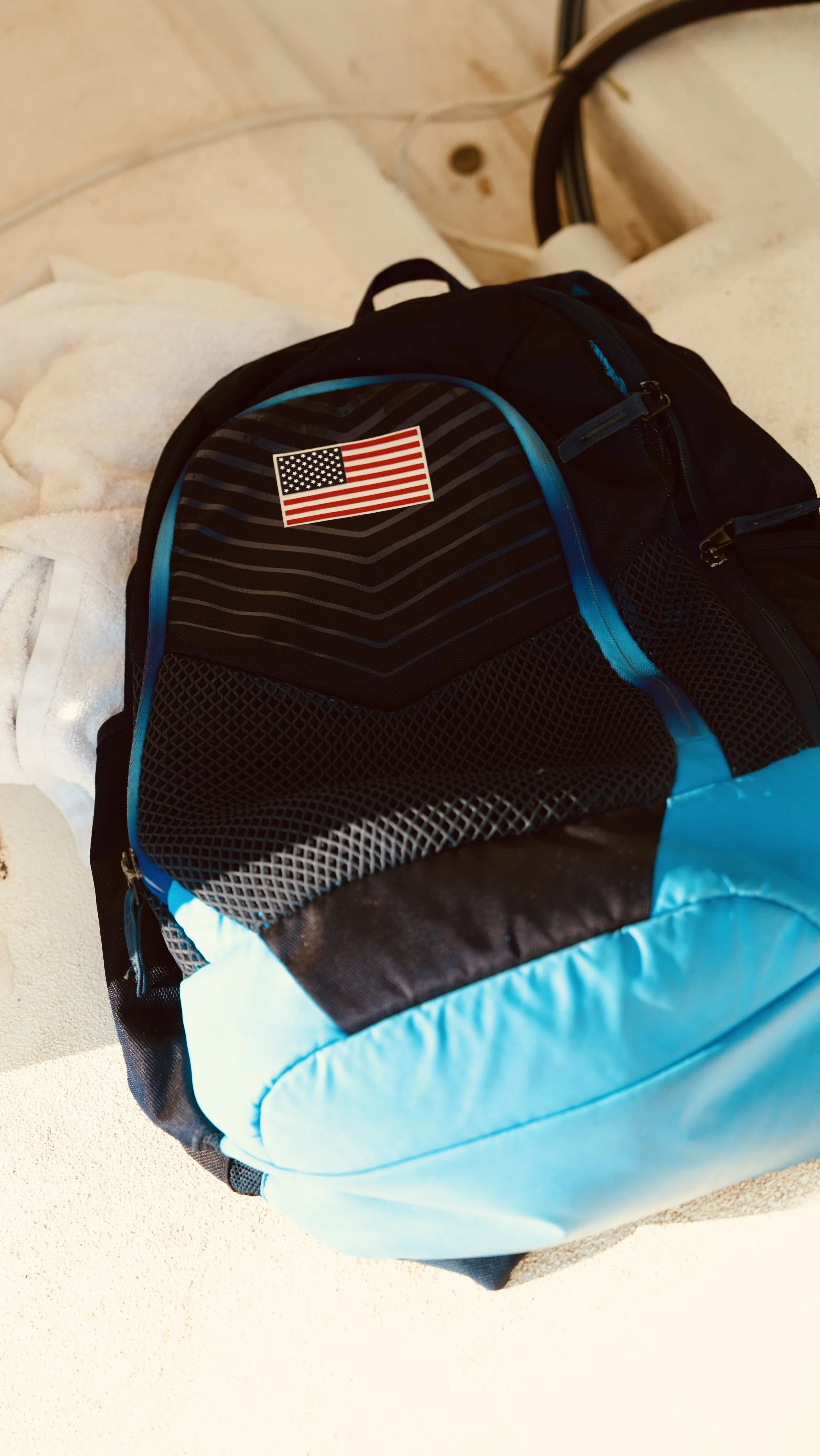 Blue and black backpack with an American flag sticker on it, placed on a beige surface.