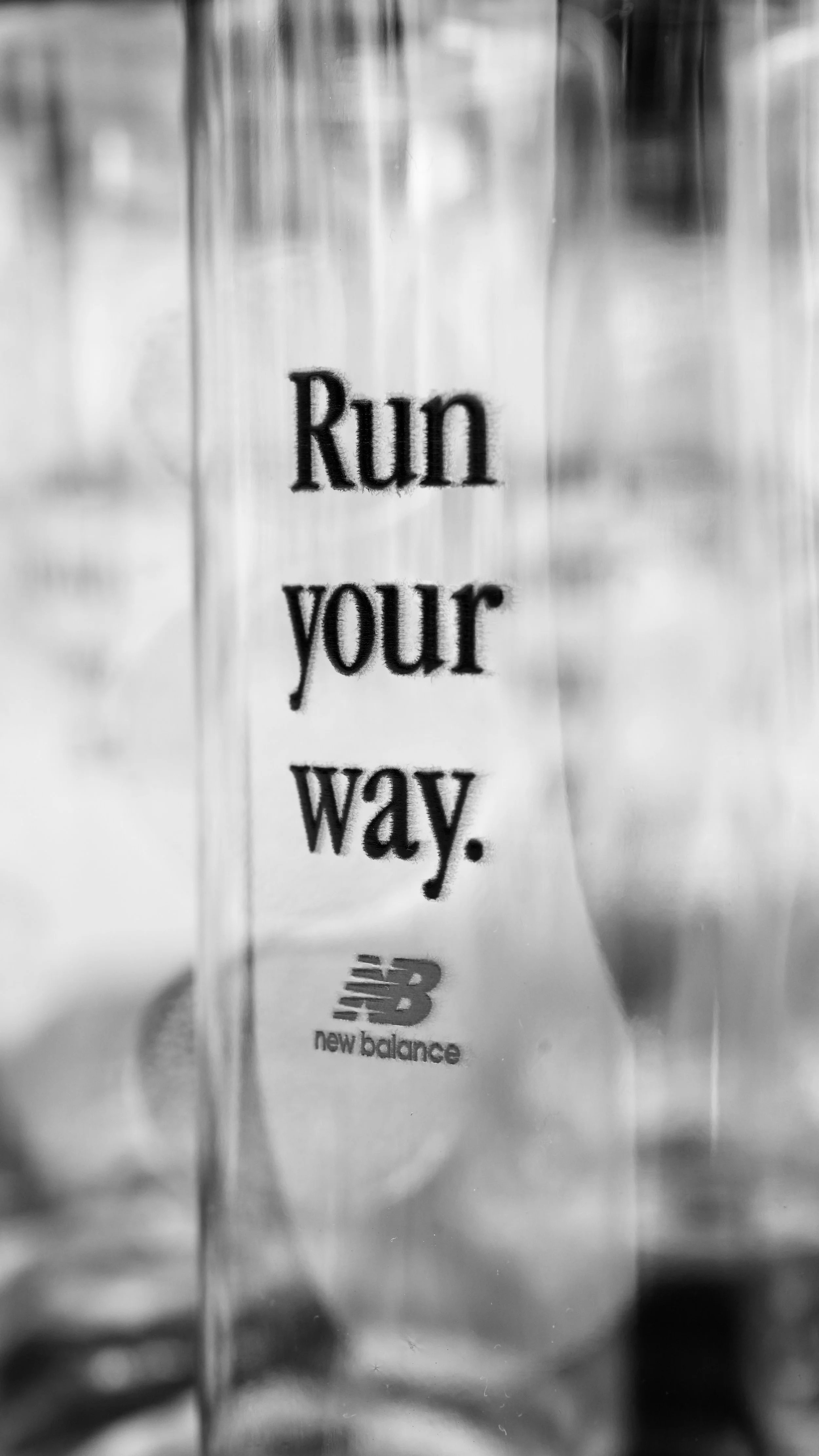 A clear plastic water bottle with the words "Run your way." printed on it, and the New Balance logo at the bottom.
