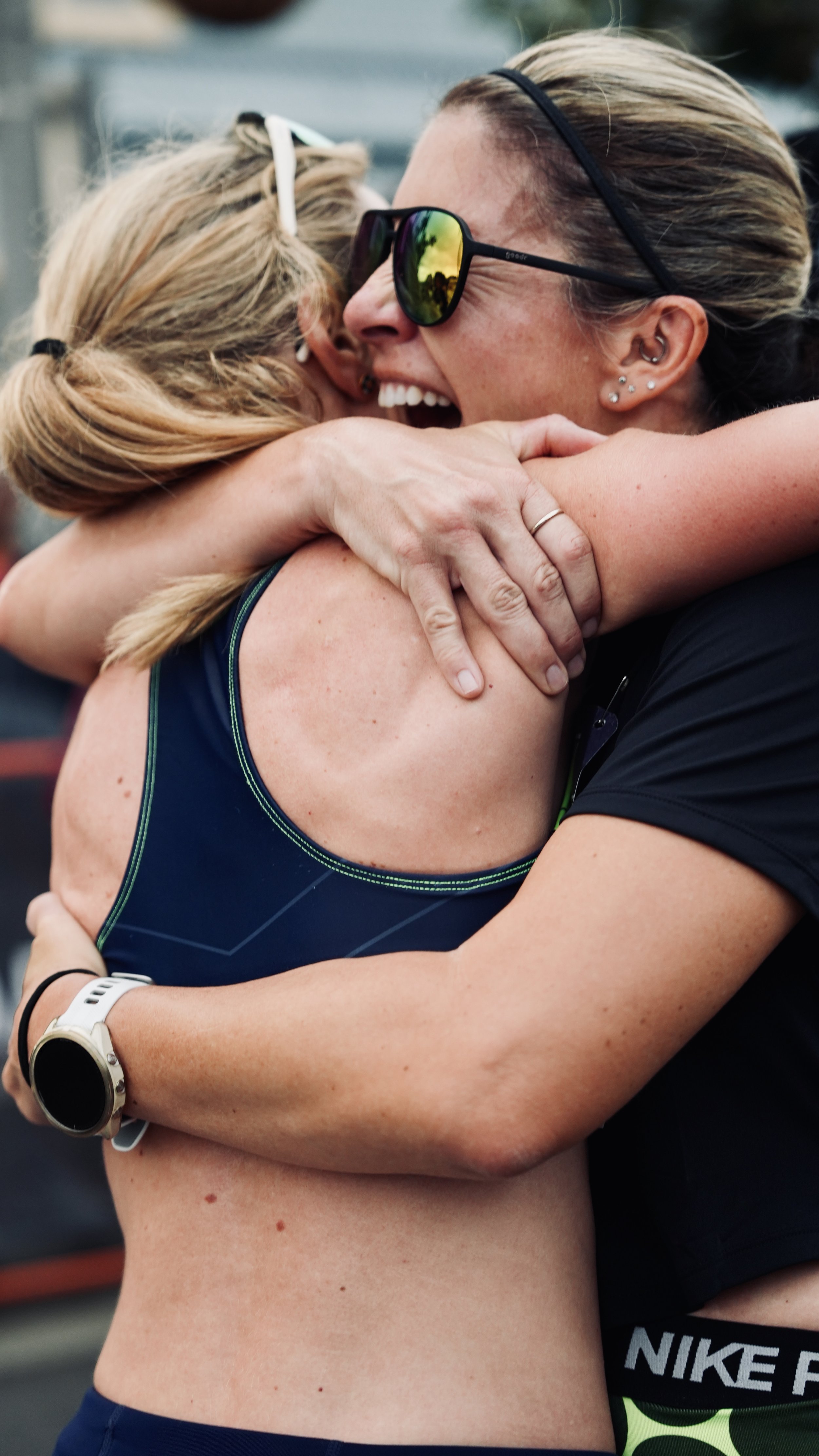 Two women hugging, one wearing sunglasses and running gear, smiling and showing happiness.