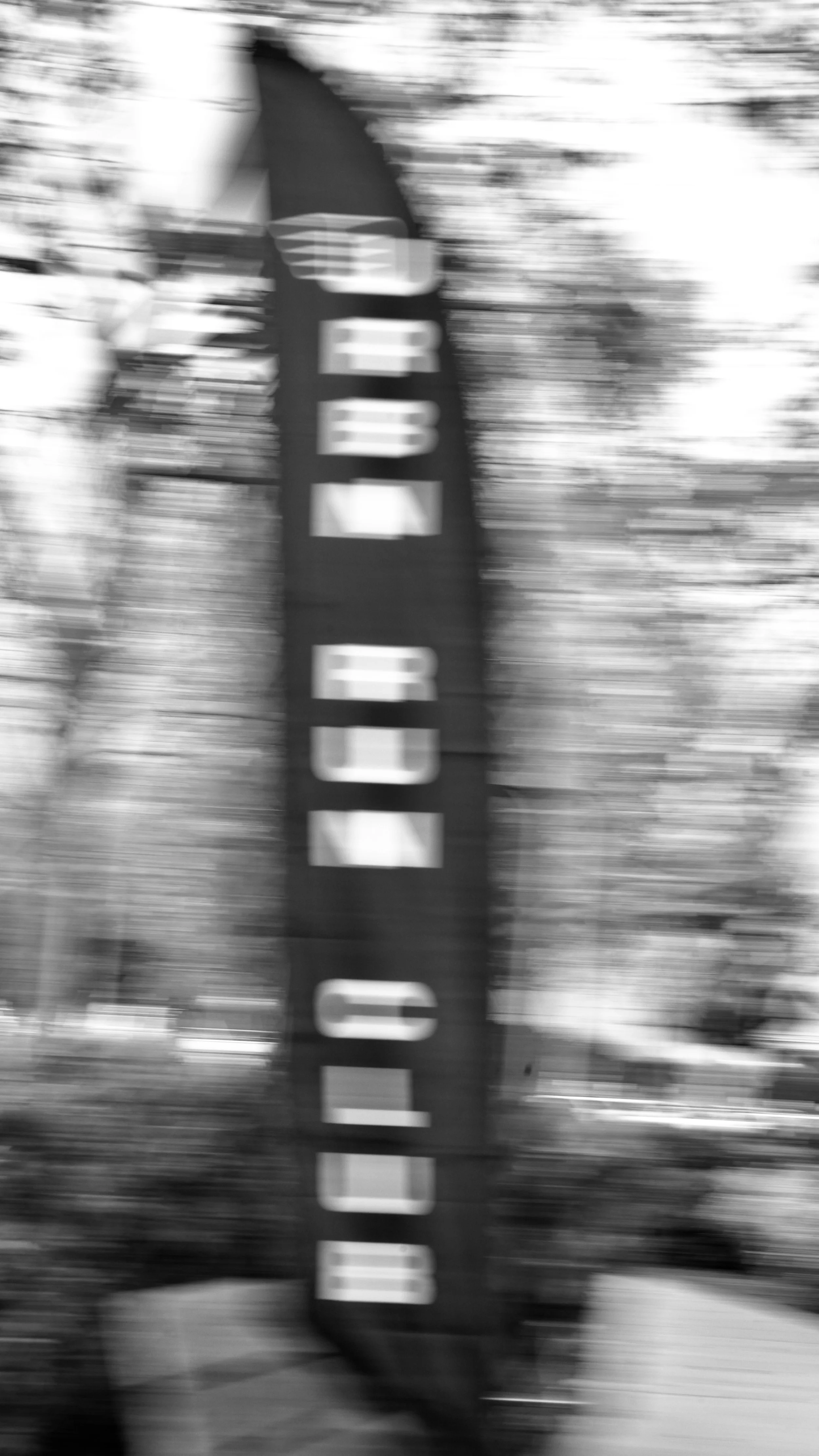 Blurry black and white photo of a vertical sign that reads 'OPEN' in large letters.
