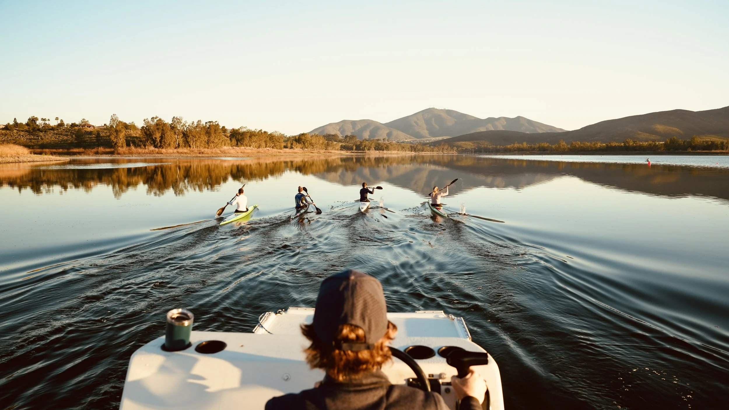 A group of five people paddleboarding on a calm lake during sunset, with mountains and trees in the background.
