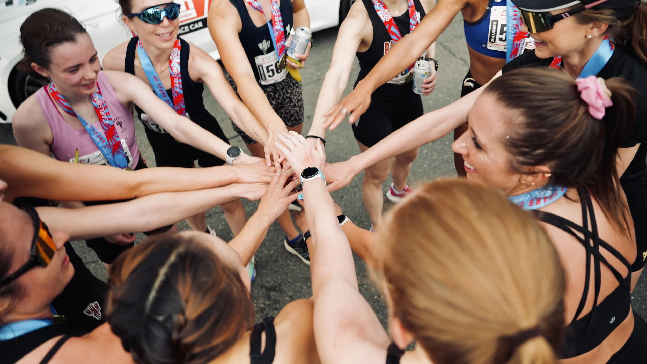 Group of women in athletic gear huddling together with hands stacked in the center, celebrating after a race.