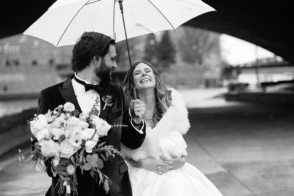 groom and bride walking closely together under an umbrella on a rainy day