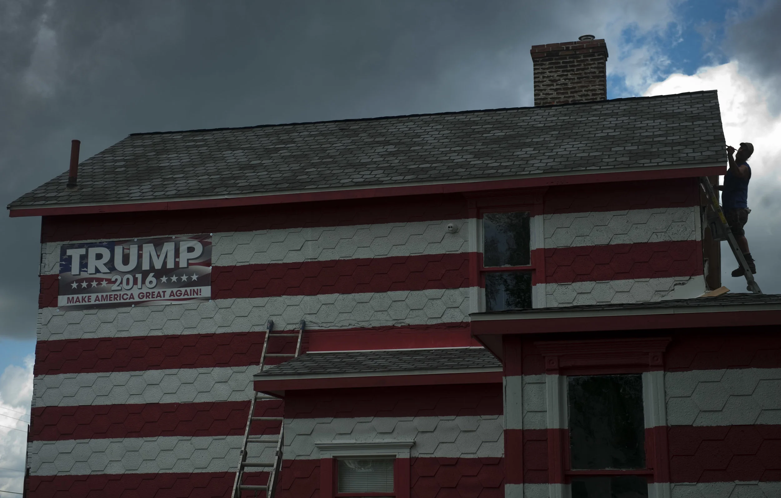 A storm cloud hovers over Dan Zak, an employee of Ligonier contractor Bob Bauer, as he finishes painting the last side of Leslie Baum Rossi's property in Youngstown on Tuesday, Aug. 16, 2016.