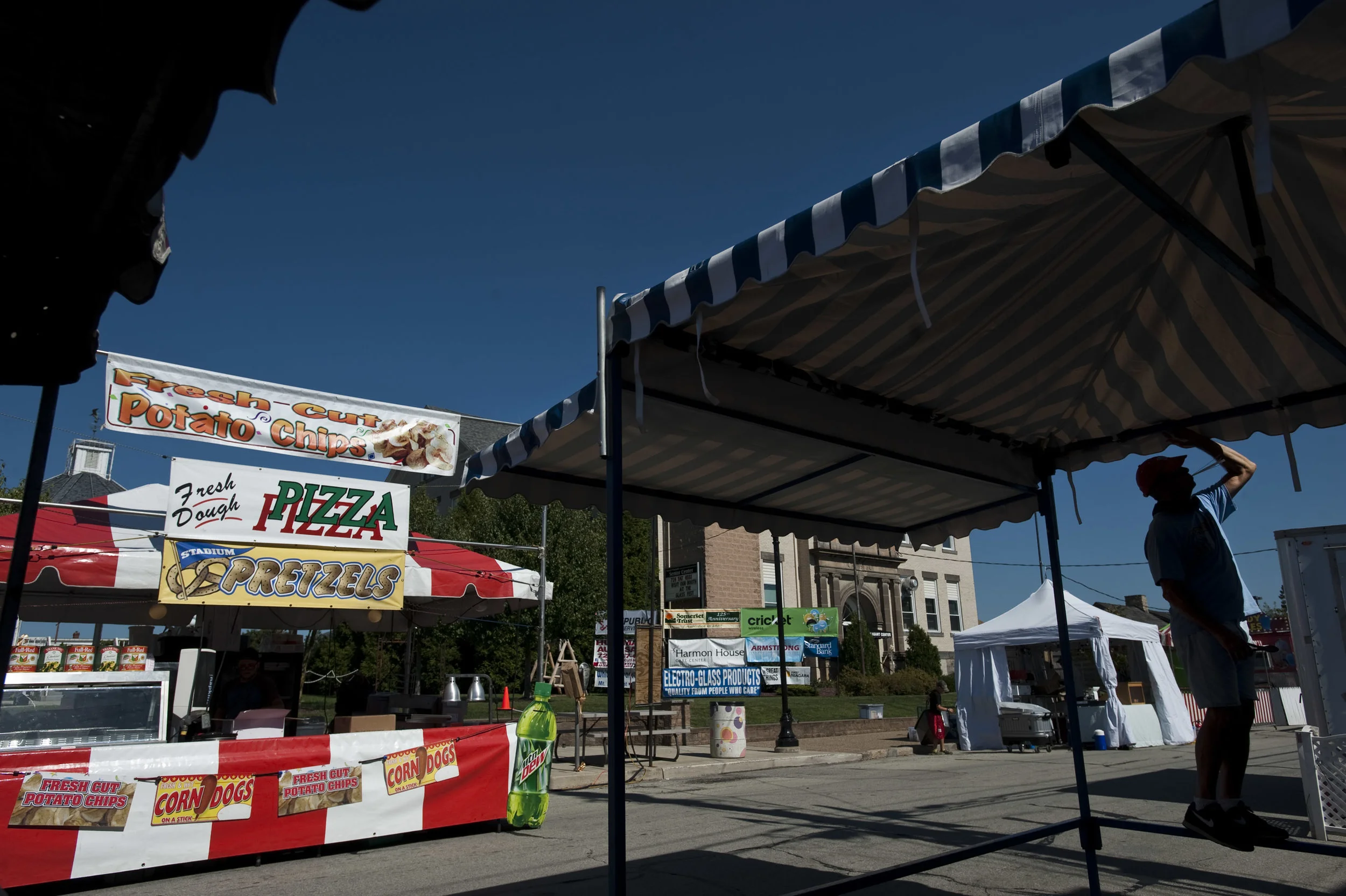 Silhouetted under the St Pius X Church booth, Joe Minick of Mt. Pleasant holds zip ties in his mouth while fastening down an awning on Thursday, Sept. 22, 2016 in preparation for the Mt. Pleasant Glass and Ethnic Festival. The festival runs Friday, …