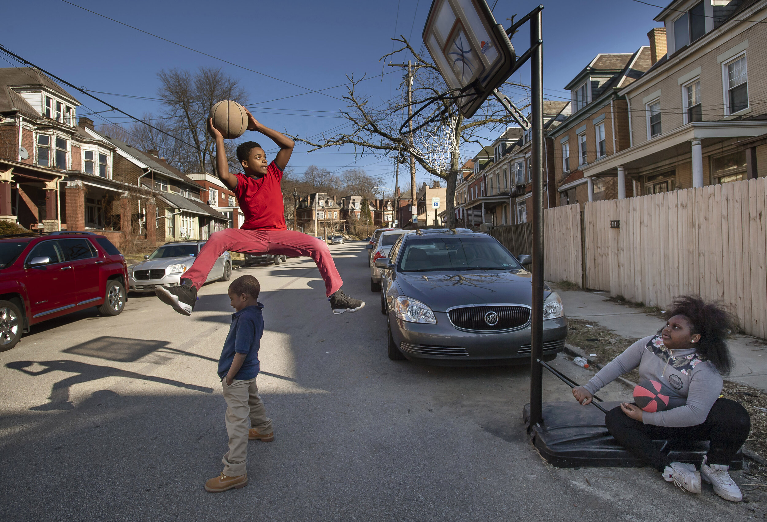  Malakai Jackson, 12, jumps over Ajaye Poindexter, 6, as Johnnaija Allen, 11, watches on as the neighborhood friends shoot hoops along Holmes Street on Tuesday, March 12, 2019, in Wilkinsburg.  