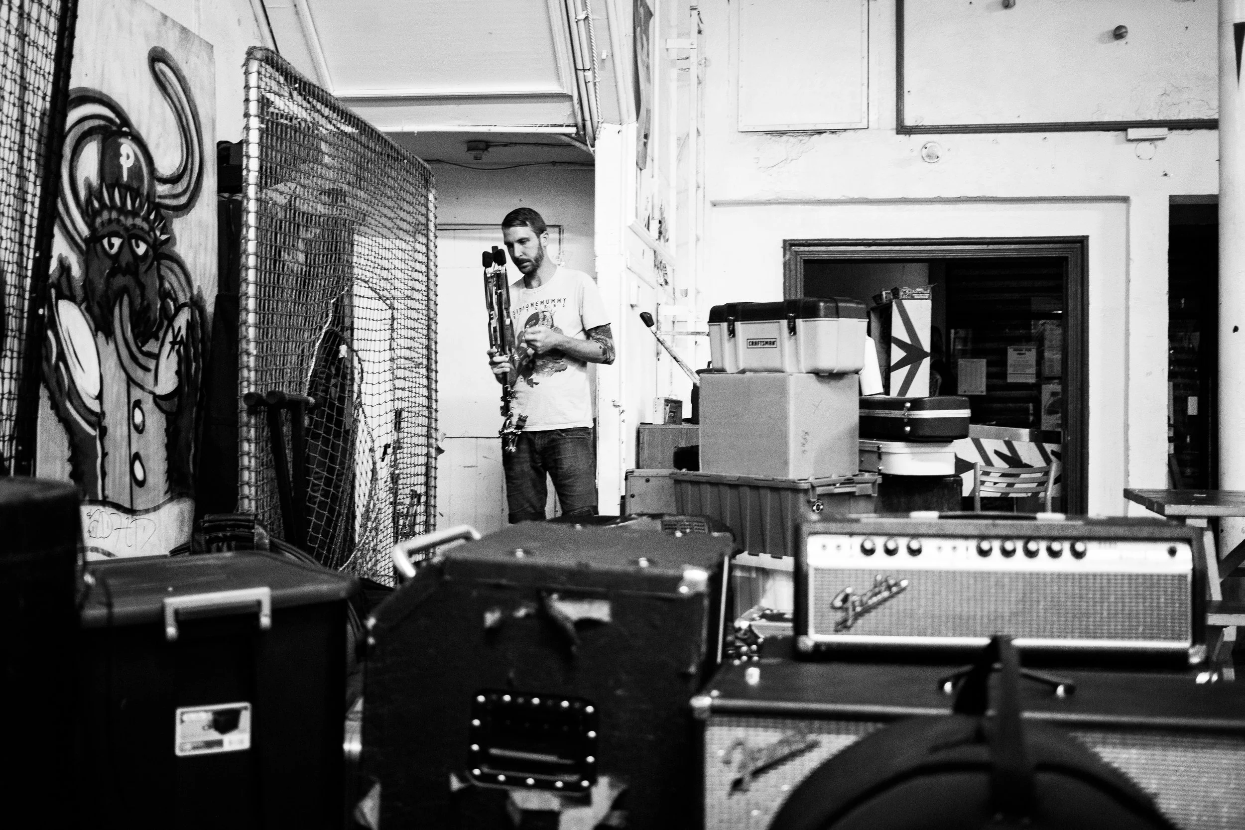 Steve begins to set up his drums among the piles of gear and merch at Everybody Hits. 