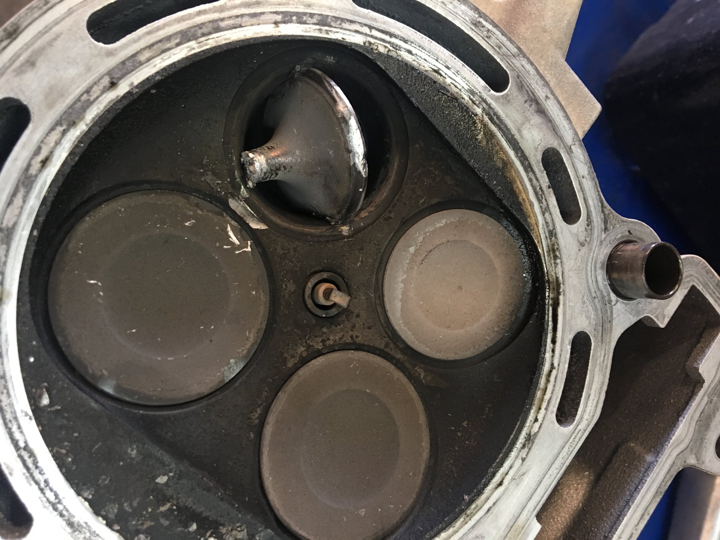 We believe what happened is that the bike was run without coolant and that exhaust valve got really hot and seized in the guide causing the piston to hit it, break it and then jam it into the head. Not a good day!