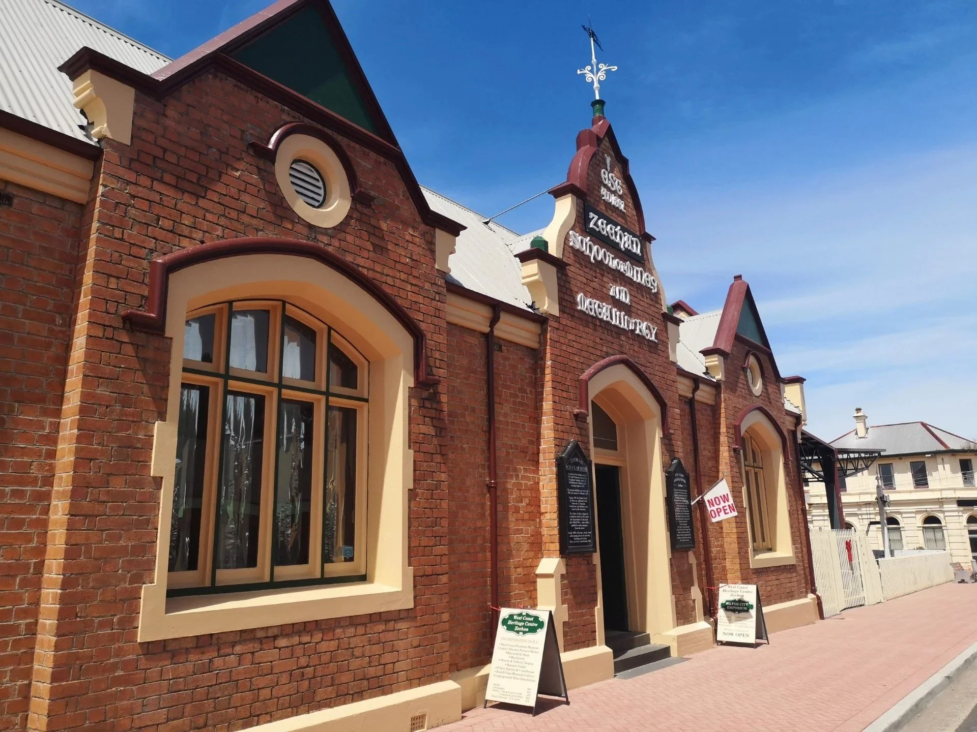 Historic red brick building with arched windows, a gabled roof, and a sign indicating it is now open, under a clear blue sky.