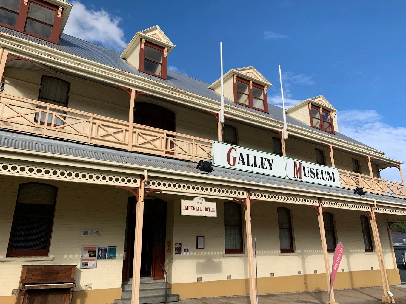 A historic building labeled as the Galley Museum and Imperial Hotel, with a porch, multiple windows, and gabled roof under a blue sky with some clouds.