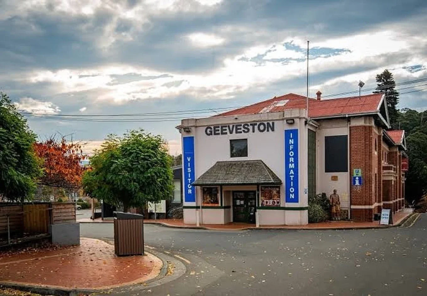 A small visitor information center named Geeveston with a sign on the front and trees around it, under a partly cloudy sky.