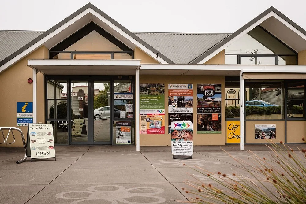Front entrance of the Delaware & Districts Folk Museum with informational posters and signs, a gift shop, and a sidewalk with decorative patterns.