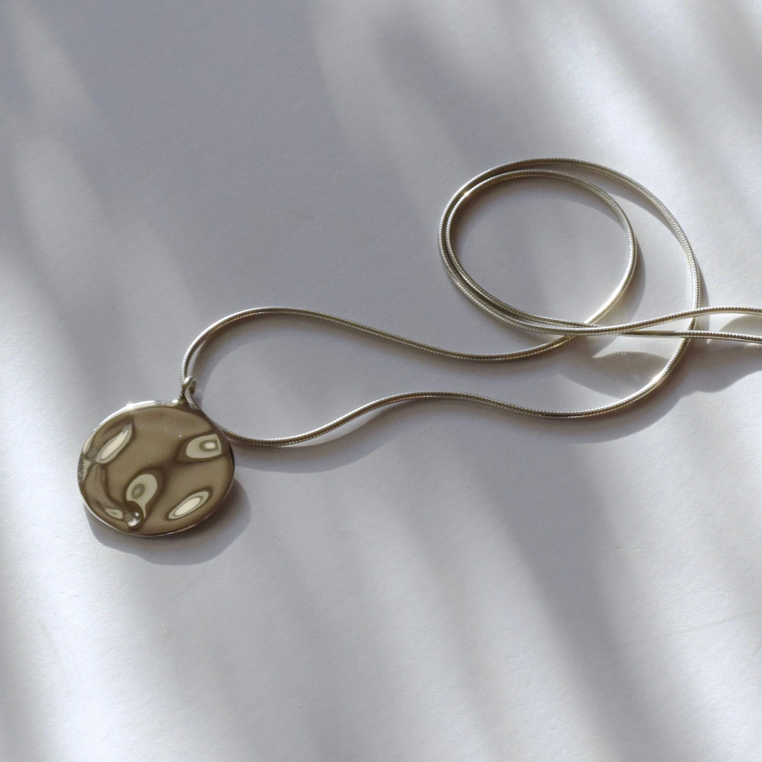 A statement pendant with water ripple texture, suspended on a liquid snake chain. It embodies the spirit of change, as a beautiful life force that carries us toward new destinations and experiences.