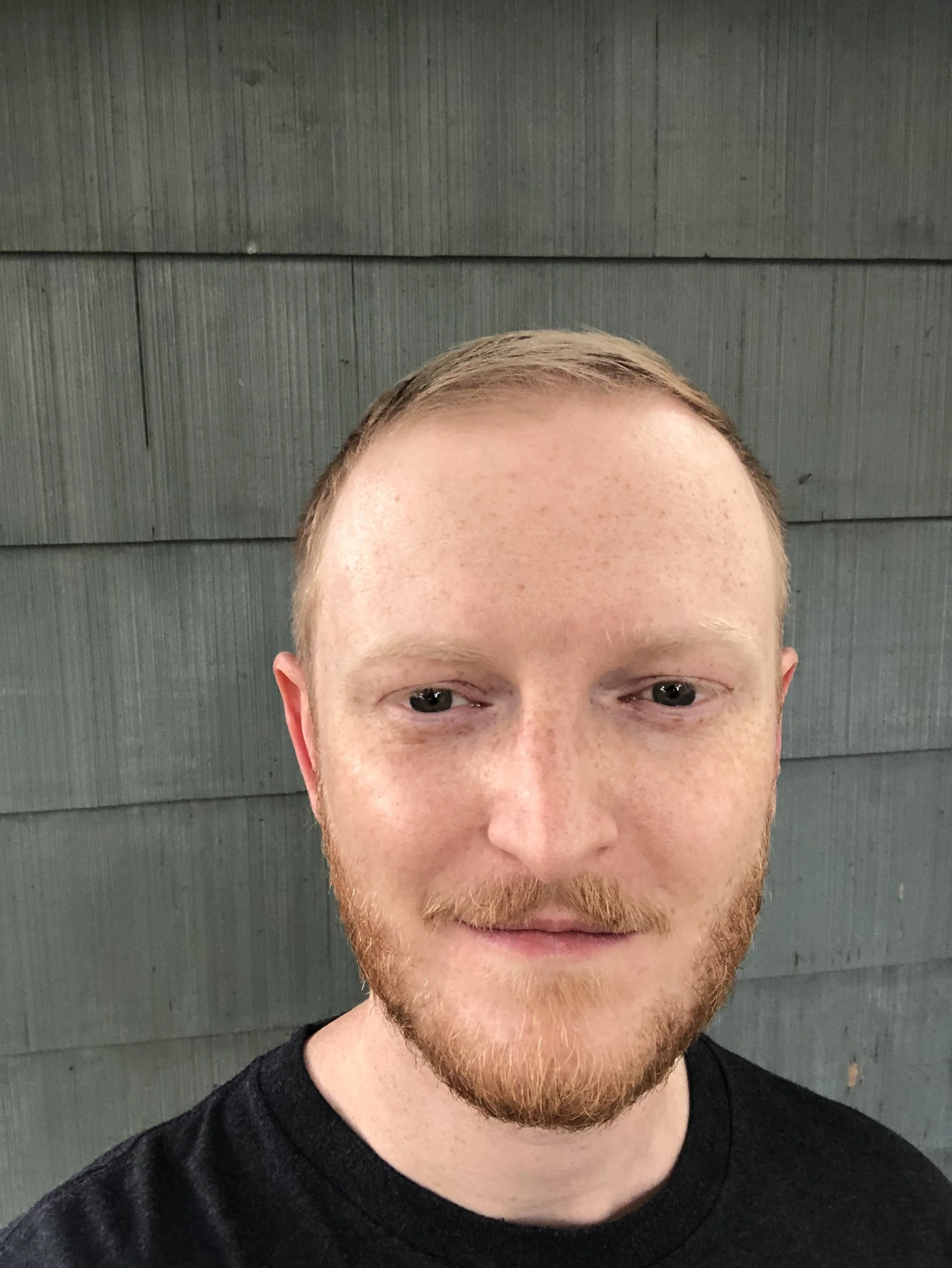 Image of a Caucasian man with short blonde hair and facial hair wearing a black t-shirt