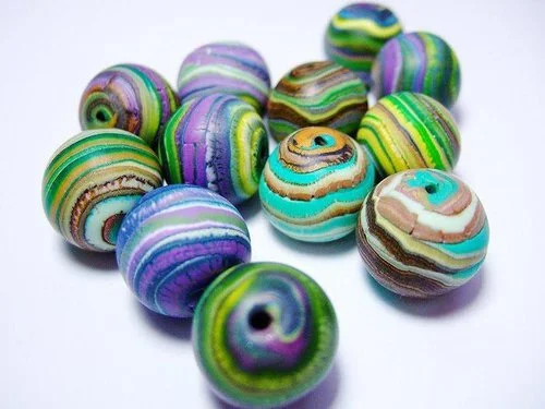 Round, multicolored polymer clay beads with swirling patterns in shades of blue, green, purple, and brown, arranged on a white surface.