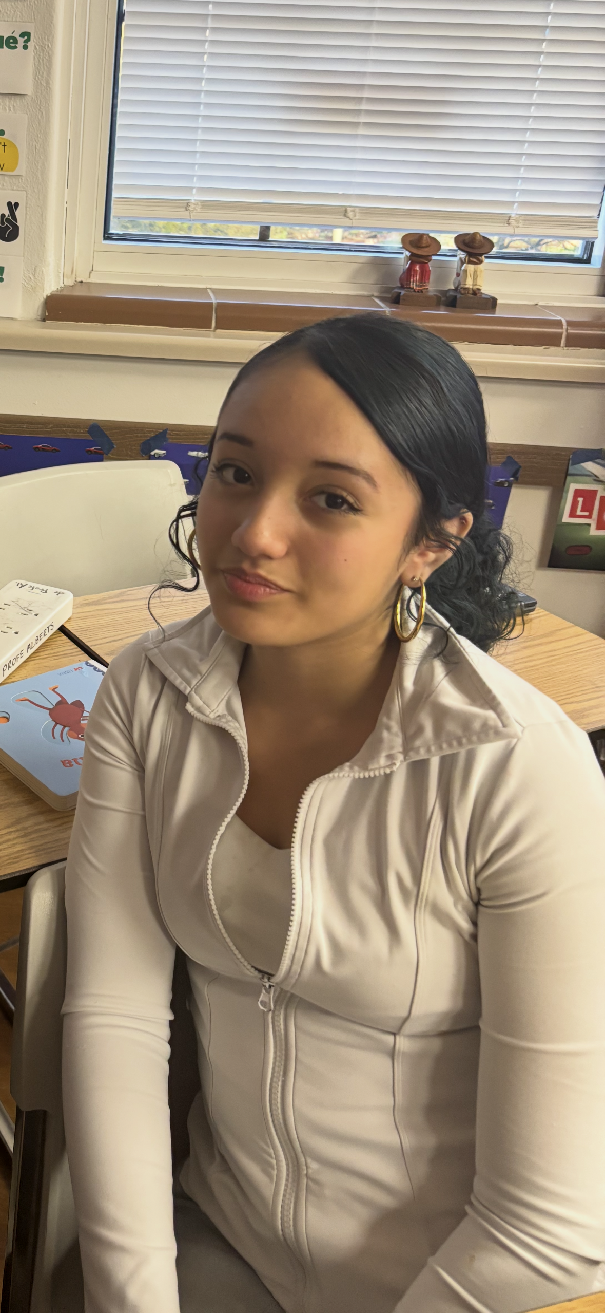 Image of Hispanic woman with black curled hair pulled back wearing a white zip up sweater
